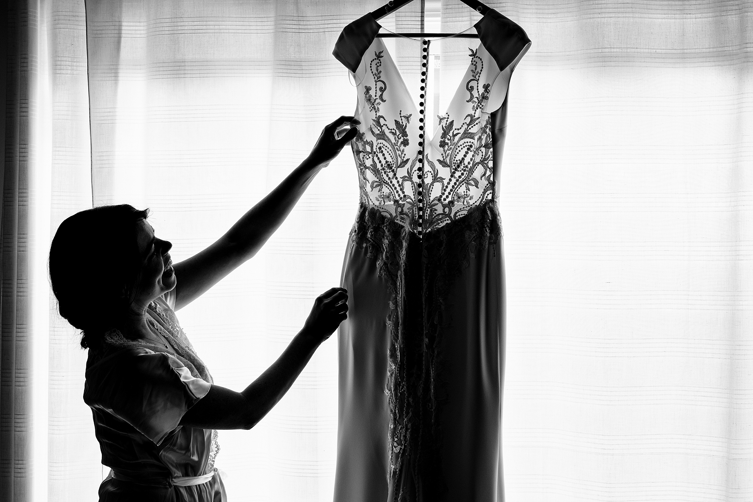A bride admires her lace dress as it hangs in a window