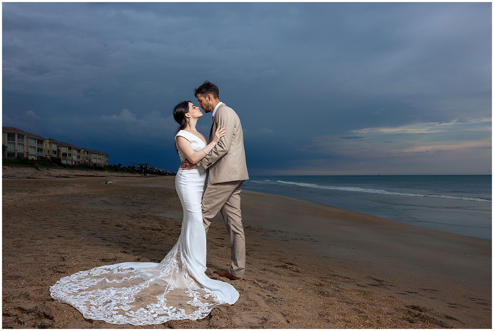 Newlyweds lean in for a kiss while standing on a beach at sunset during their serenata beach club wedding