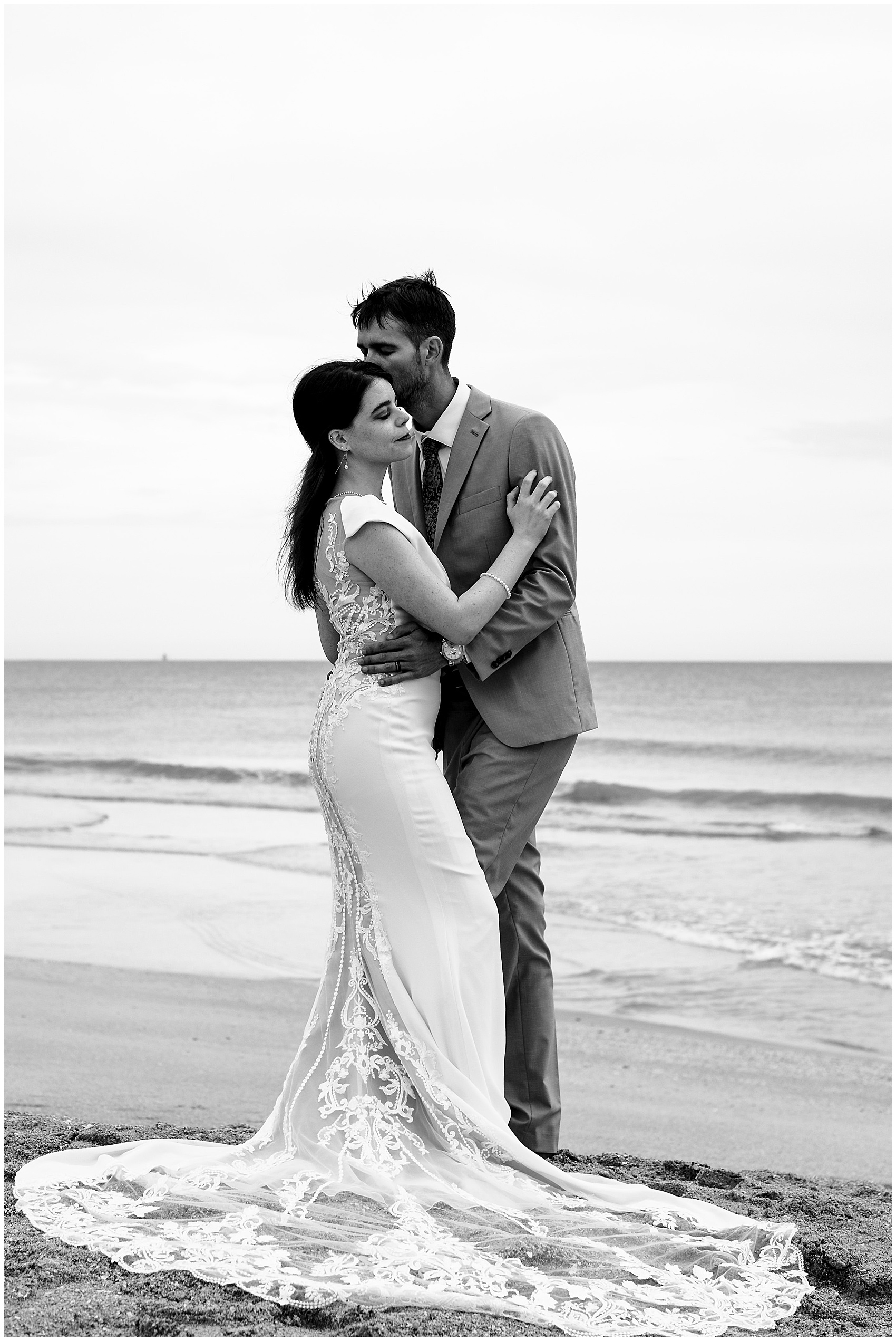 Newlyweds stand together on a beach with the train fully fluffed at their serenata beach club wedding