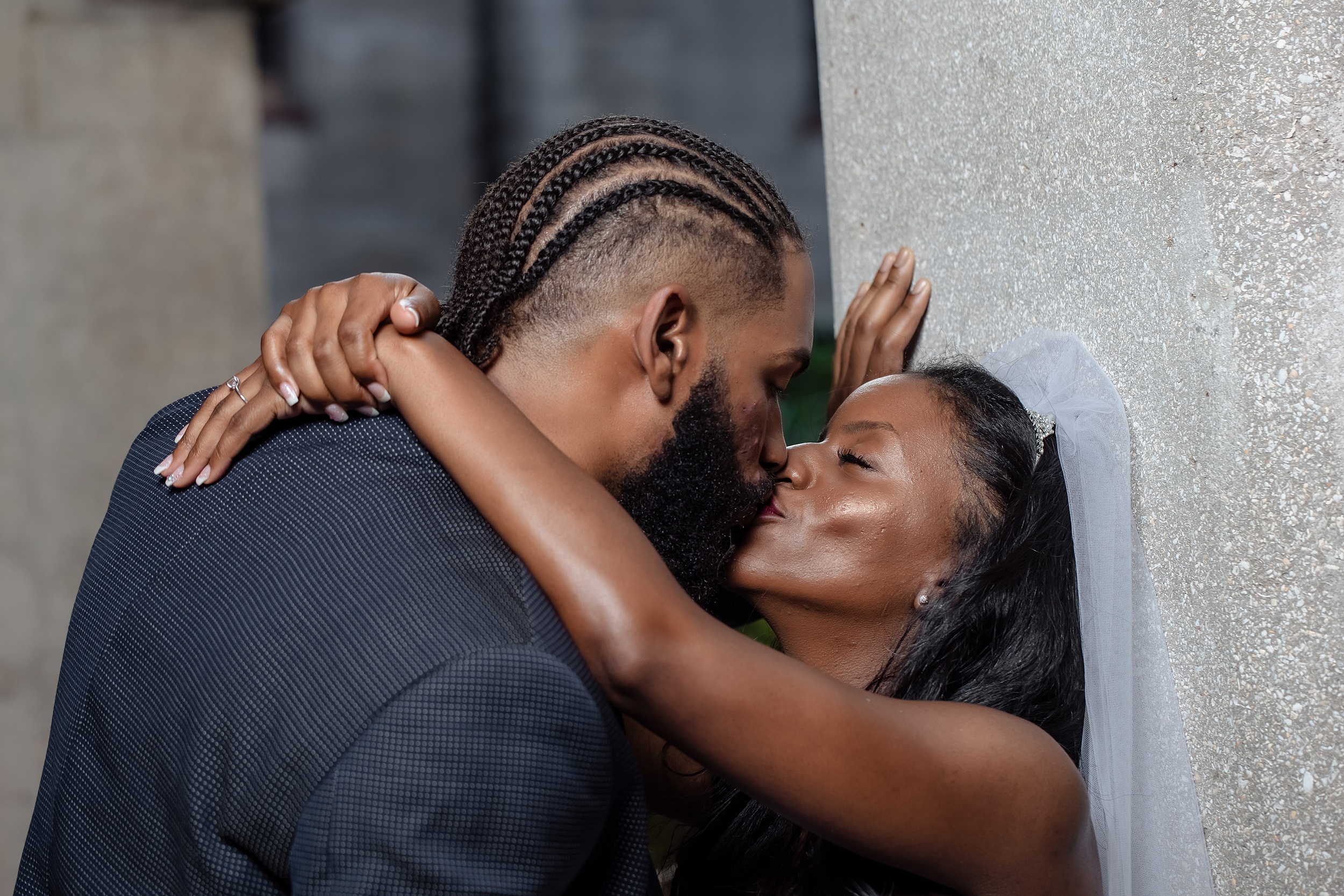 Newlyweds kiss while leaning on a concrete wall
