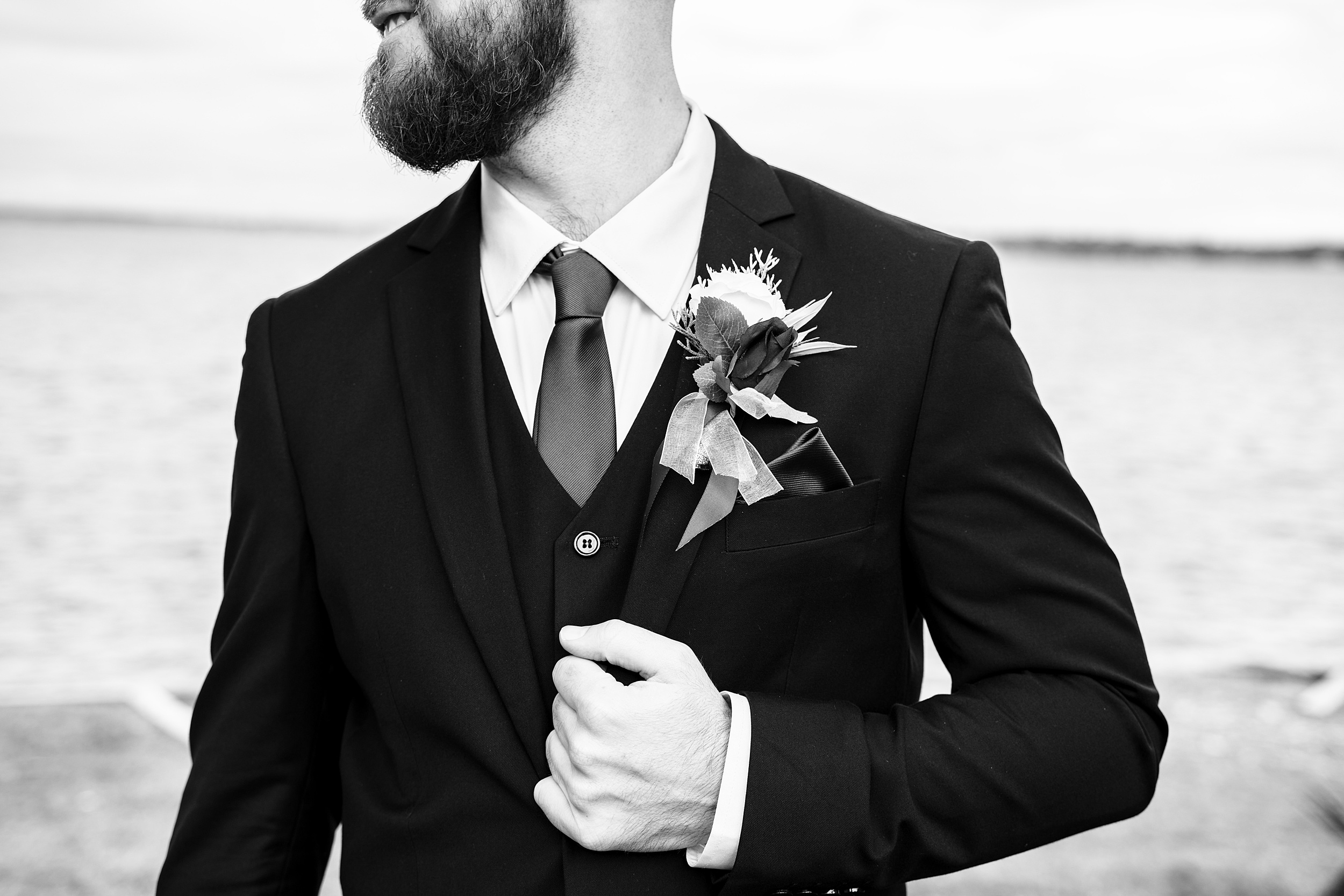 A groom stands by the water holding his lapel at his 1010 west wedding