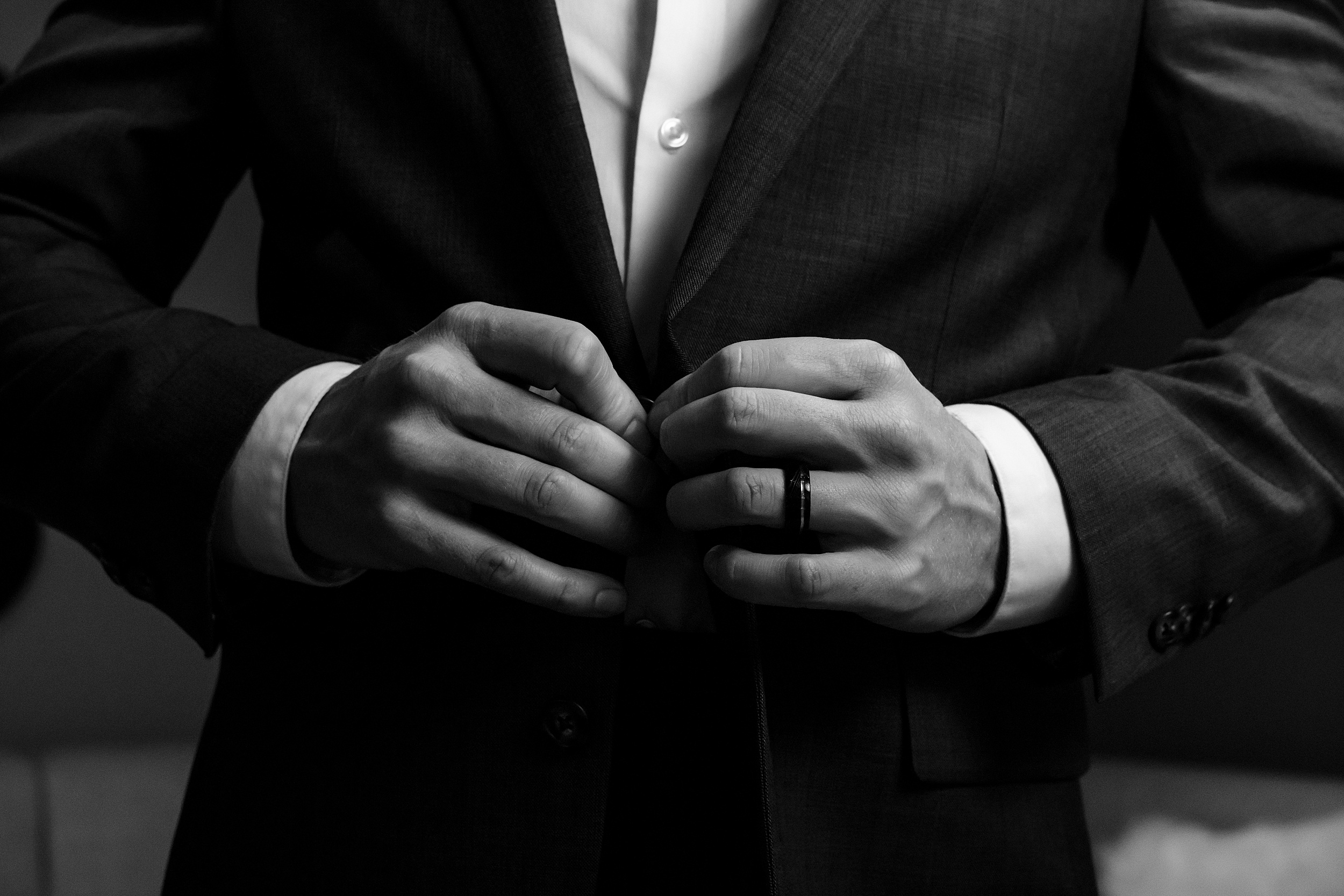 Details of a groom buttoning his suit in dramatic lighting
