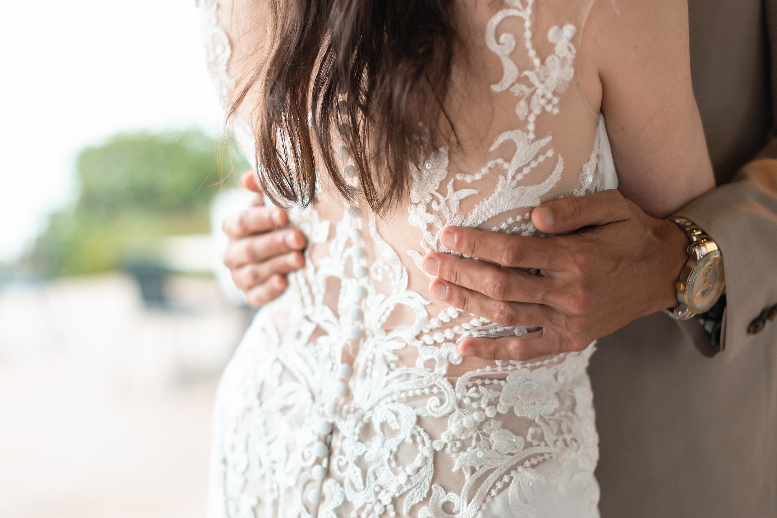 Details of a bride's embroidered lace dress while hugging her groom at their bramble tree estate wedding