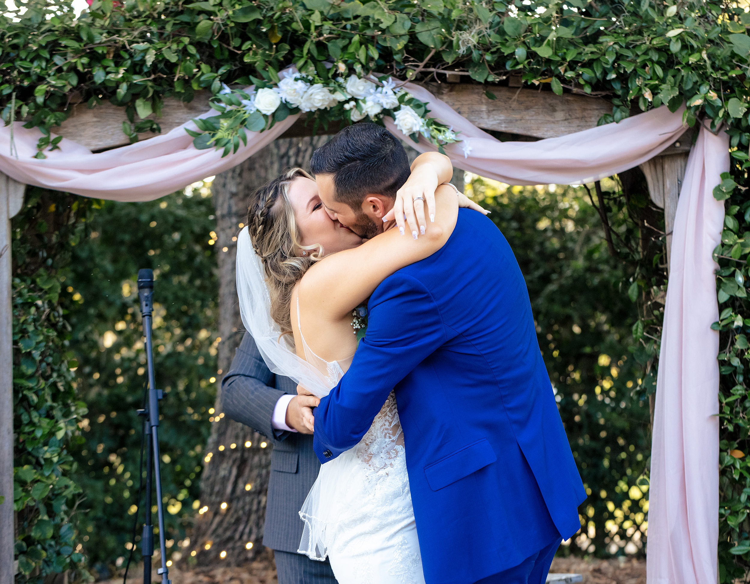 Newlyweds kiss under a wooden vine covered arbor at their Ever After Farms Weddings ceremony