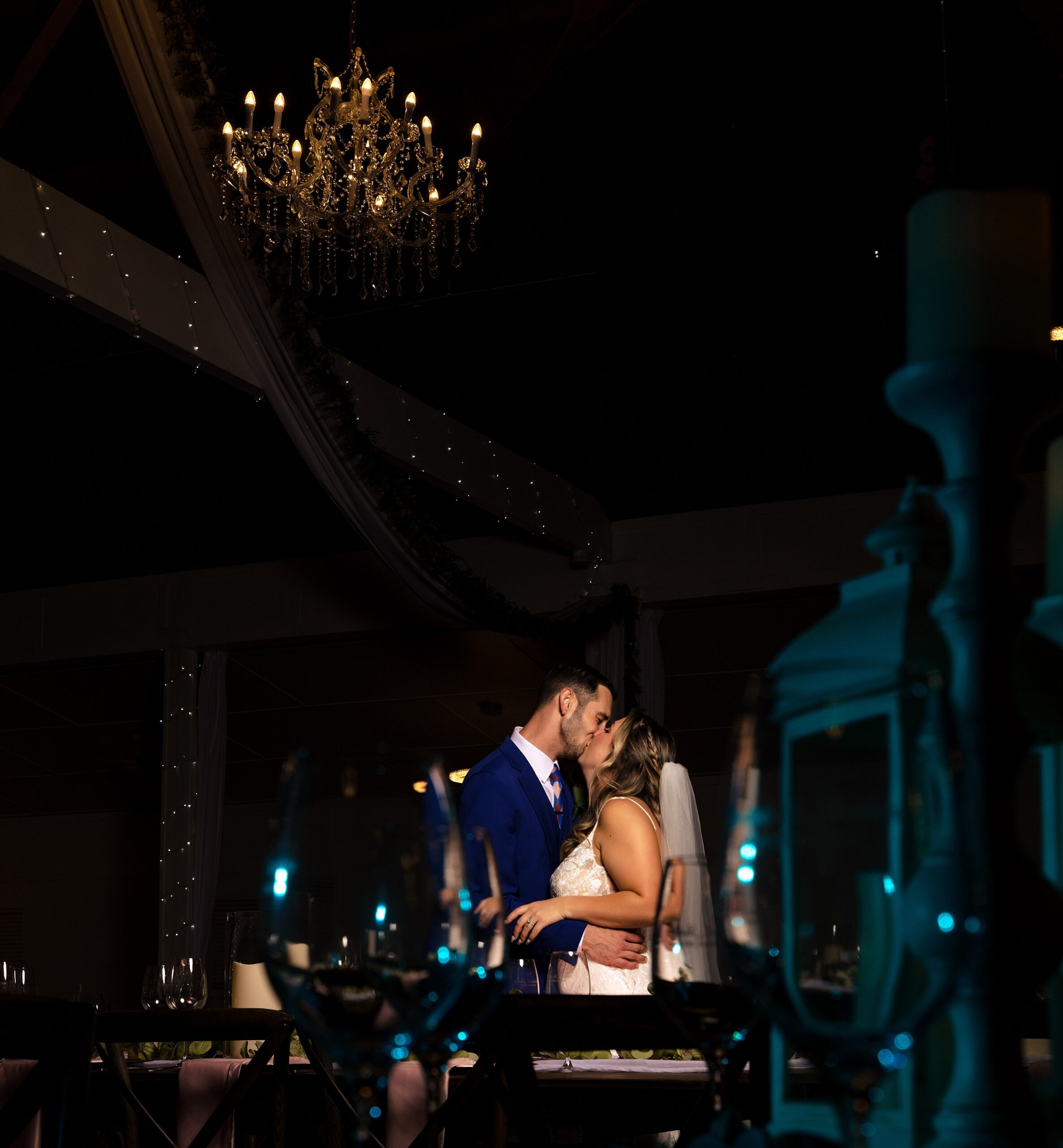 Newlyweds sneak an intimate kiss under a chandelier at their Ever After Farms Weddings