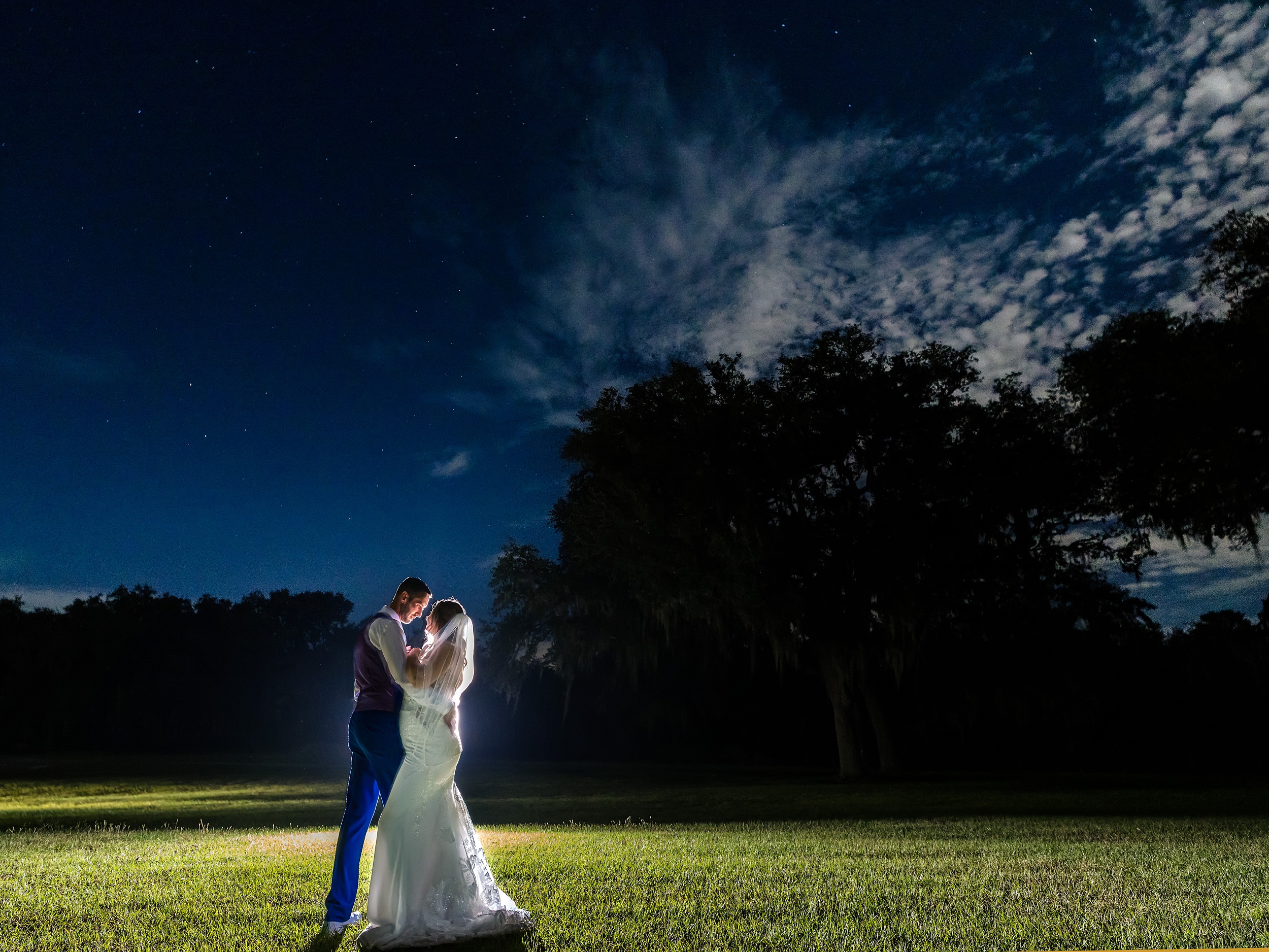 Newlyweds lean in for a dramatic kkiss in an open field under the stars at their Ever After Farms Weddings