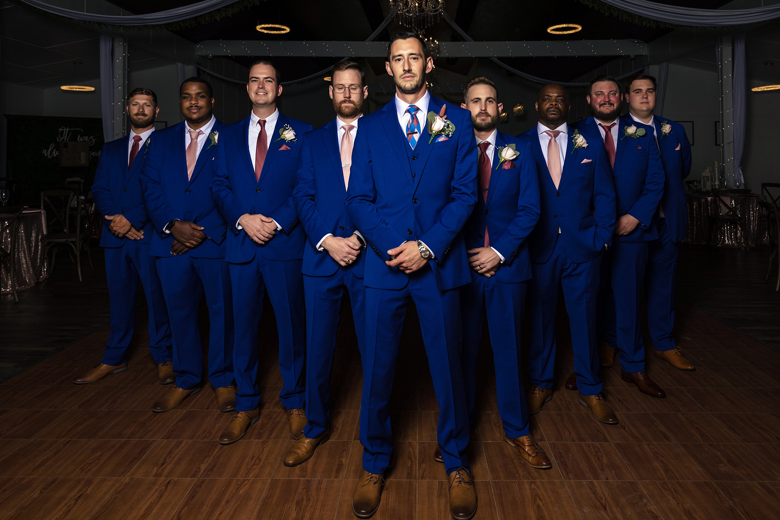 A groom stands with his large party of groomsmen with hands crossed in a V formation