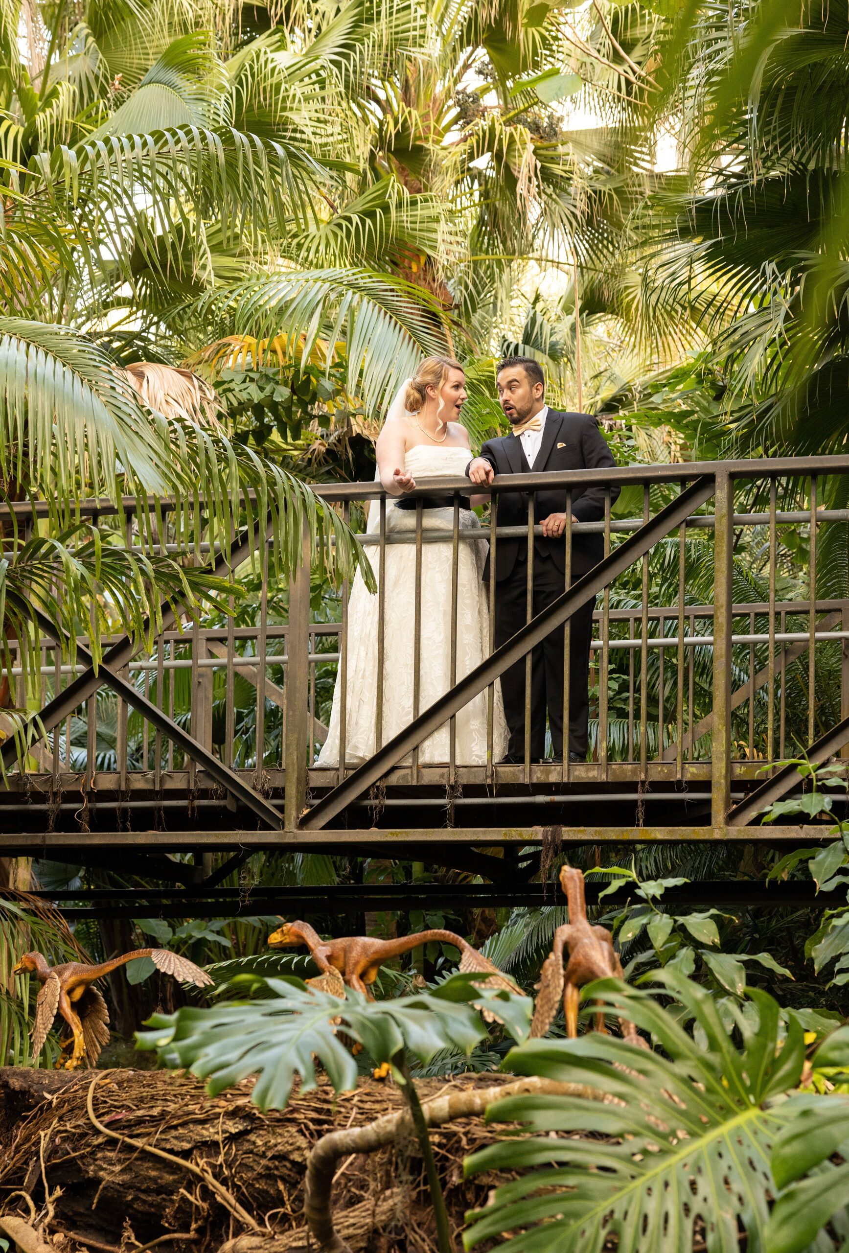 Newlyweds make special faces while standing on a bridge overlooking some dinosaurs running beneath them at their leu gardens wedding