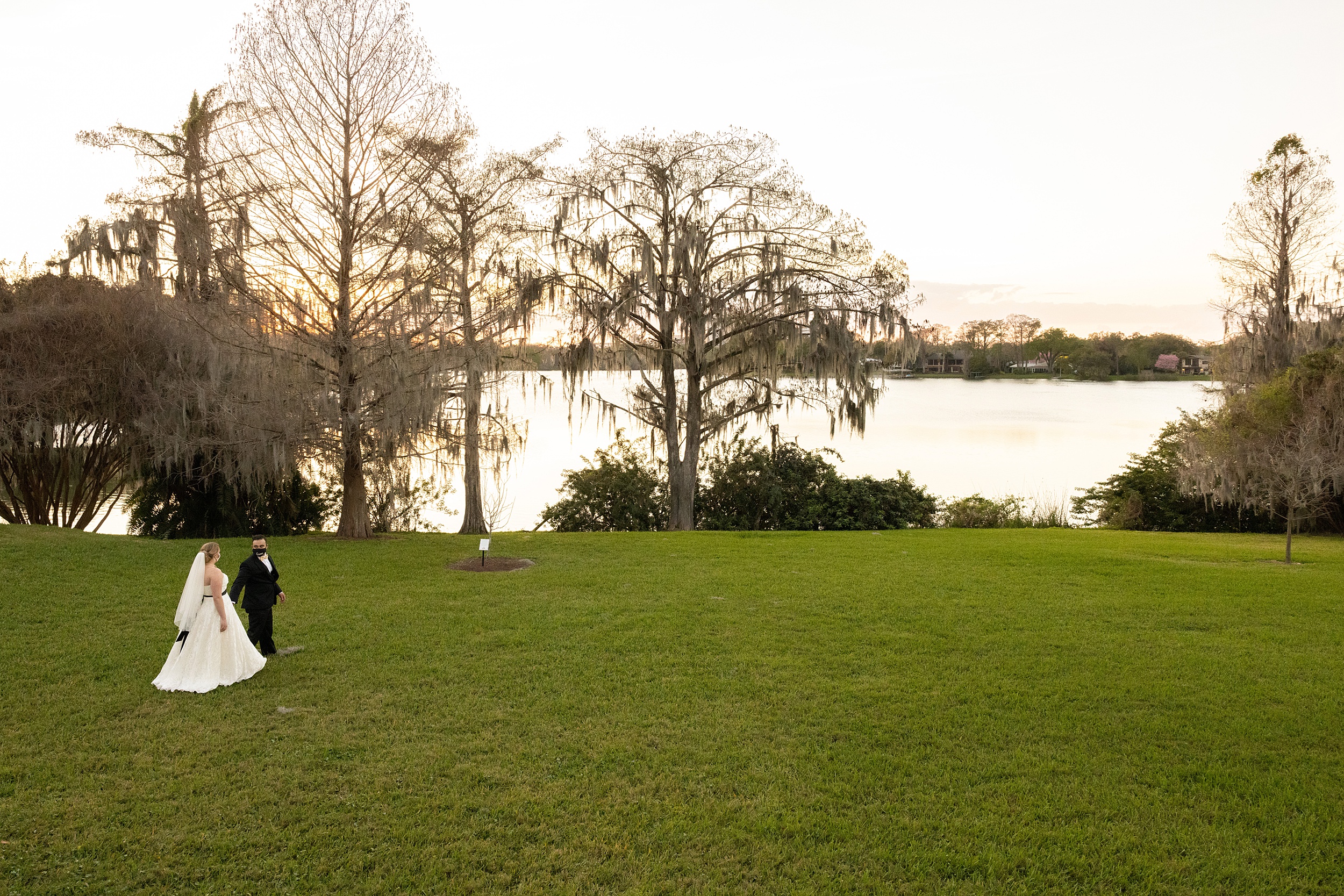 Newlyweds walk hand in hand through a lawn on a lake