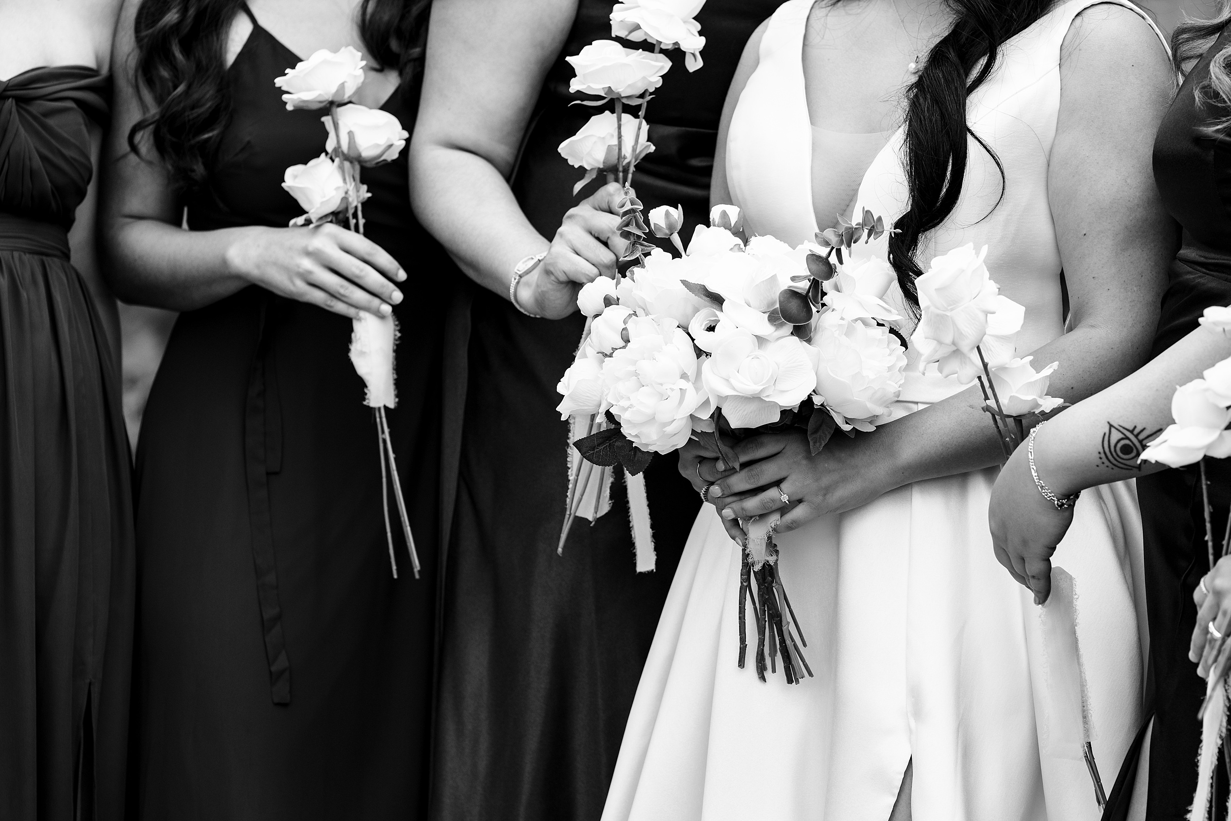 Details of a bride holding a bouquet of white roses while surrounded by her bridesmaids