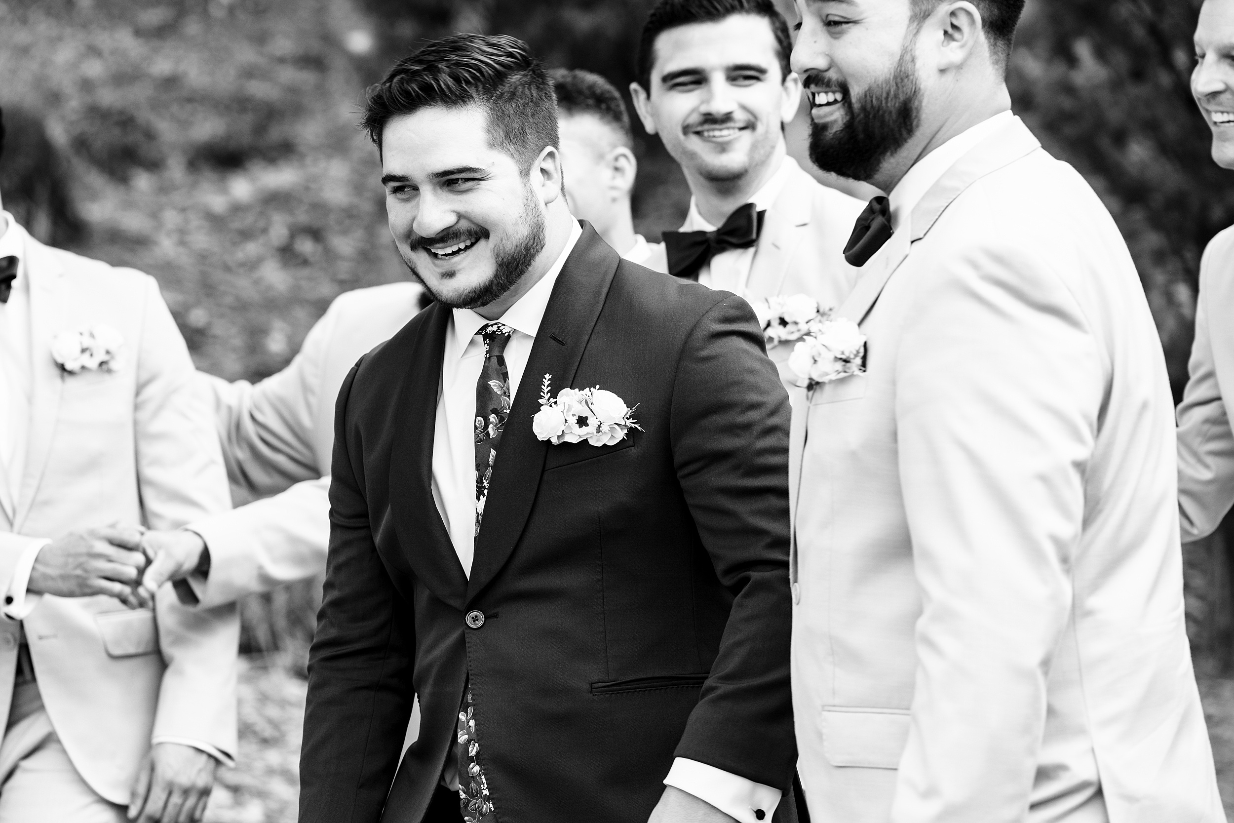 A groom smiles big while walking with his groomsmen through a lawn at his mission inn resort wedding