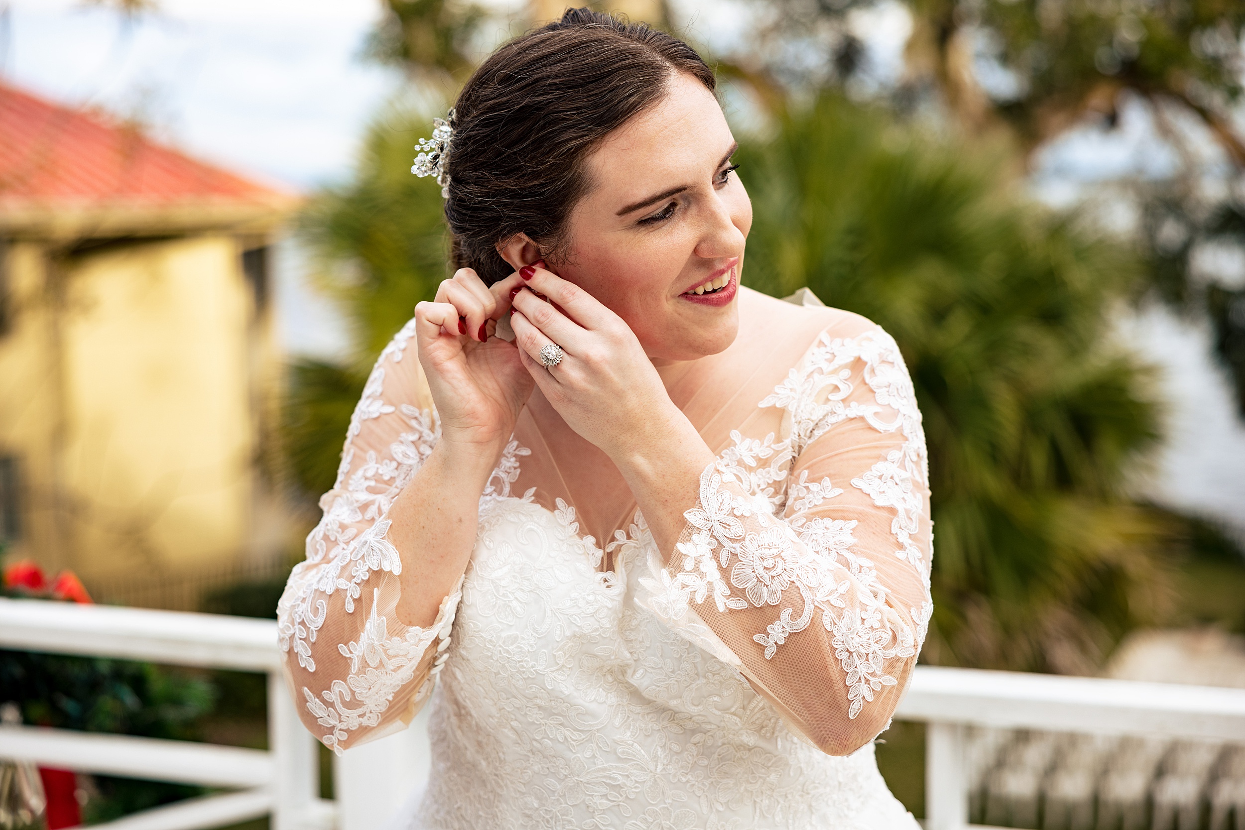 A bride in a lace embroidered dress puts on an earring