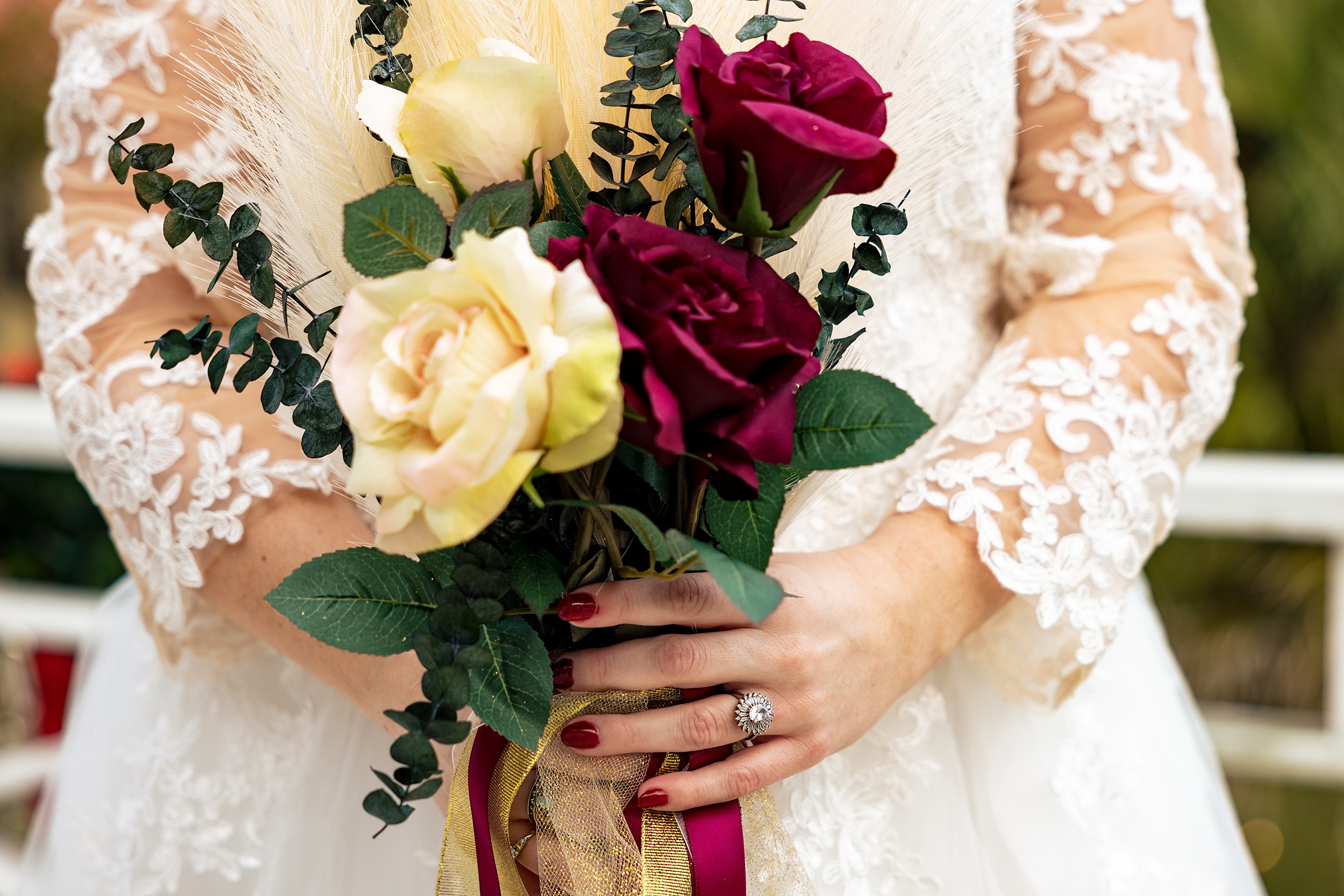 Details of a bride in a lace dress holding her white and red bouquet during her paradise cove wedding