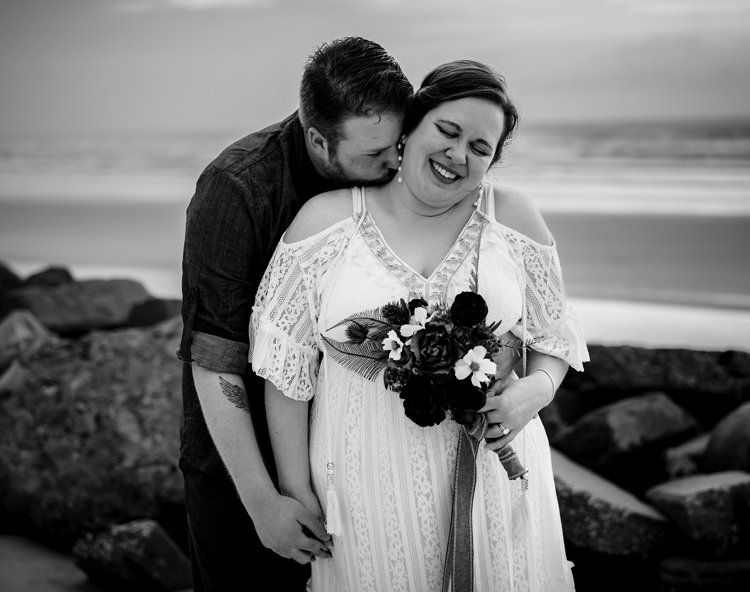 A groom kisses the neck of his bride as she laughs on a beach at sunset at their st augustine beach wedding venues