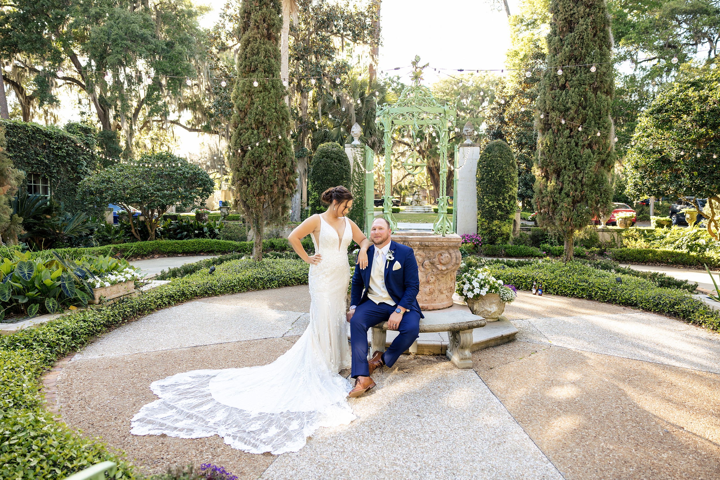 A groom in a blue suit sits on a garden bench while his bride leans on his shoulder at one of the st augustine garden wedding venues