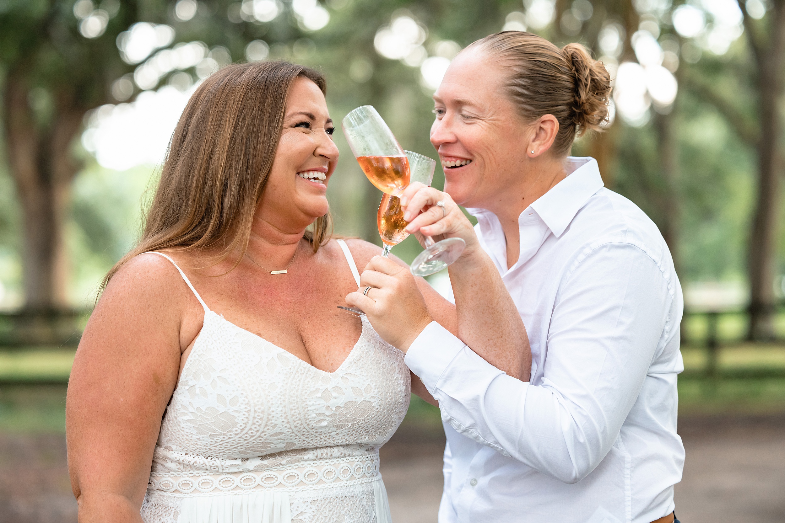 Newlyweds toast with pink champagne outside under some trees