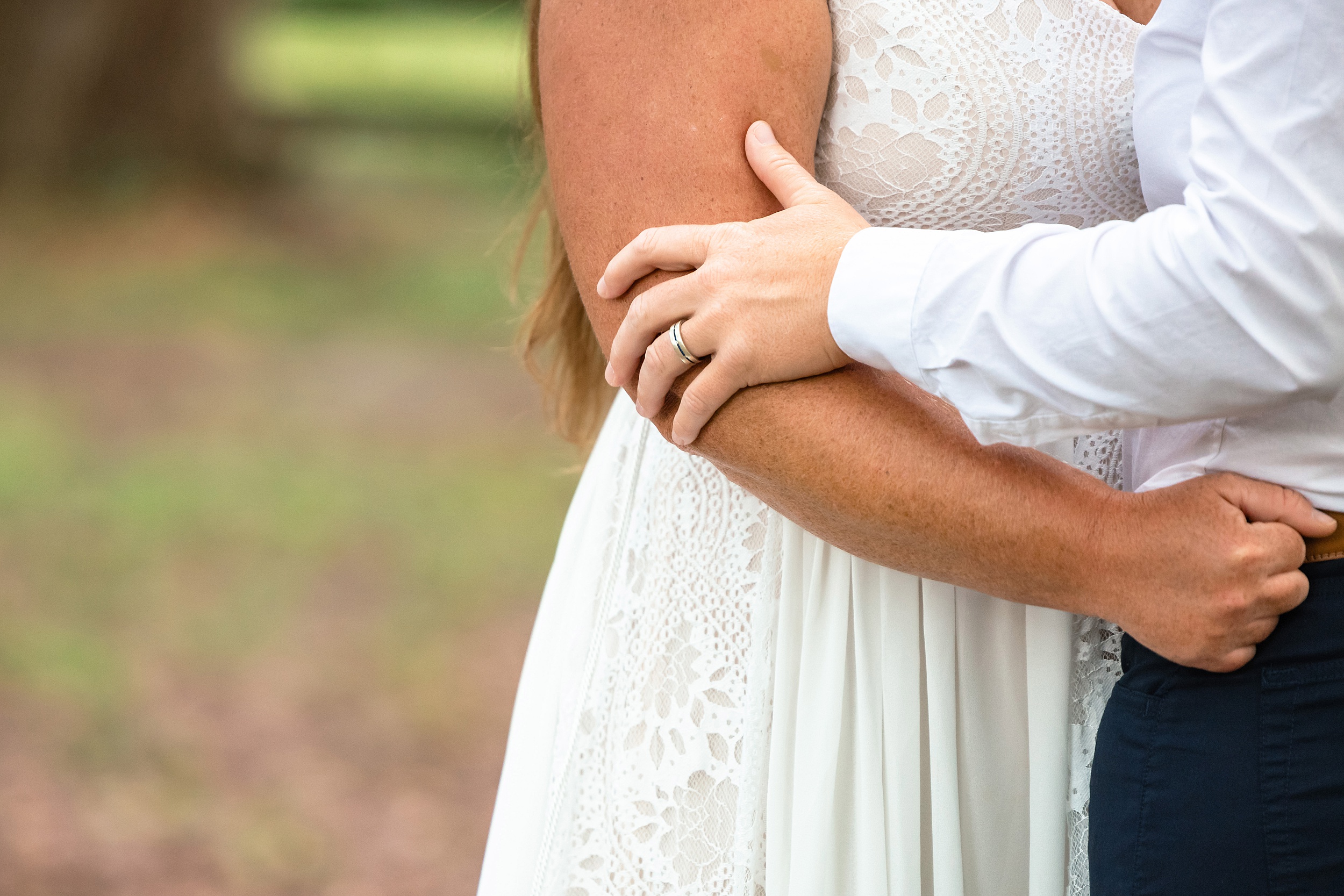 Newlyweds hold on to each other while standing outside under some trees