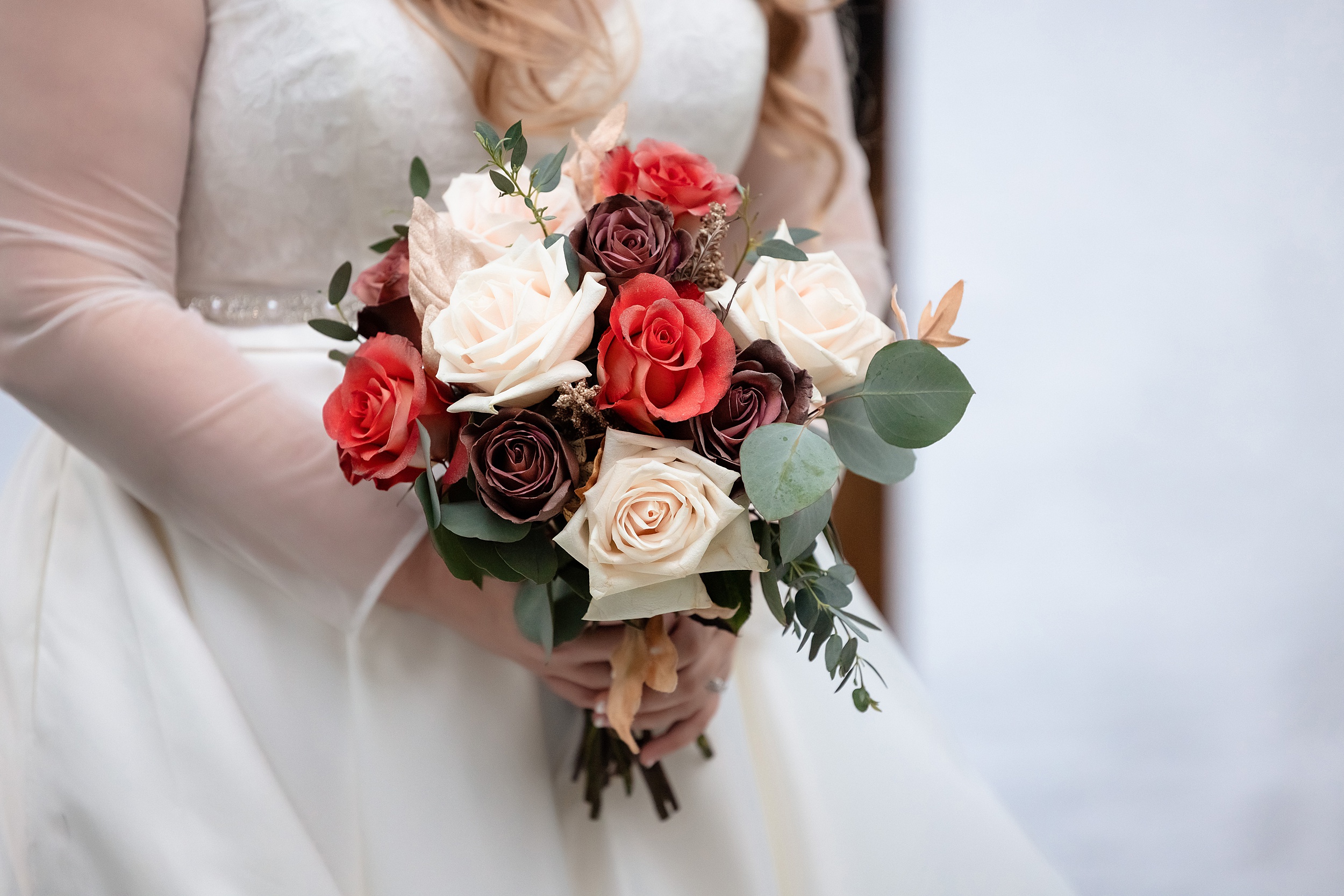 Details of a bride's bouquet with red, purple and white roses at her the enchanting barn wedding