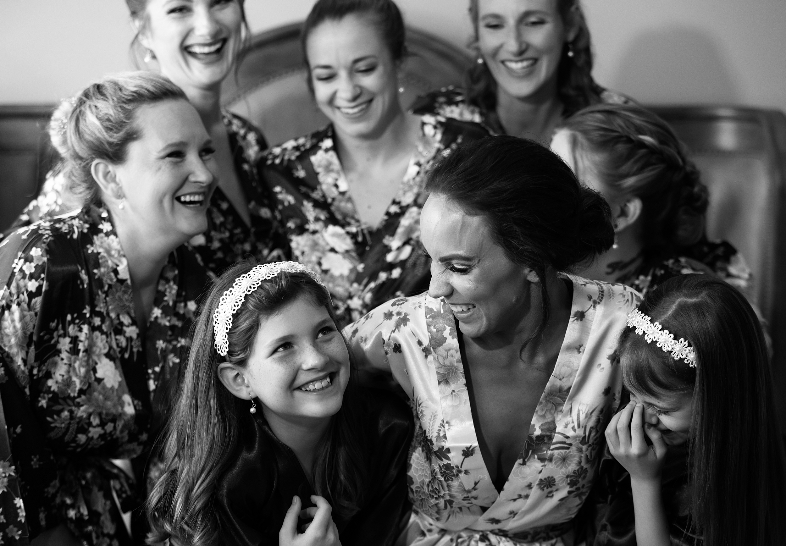 A bride laughs with her bridesmaids and flower girls while sitting on a bed in pajamas at her the howey mansion wedding