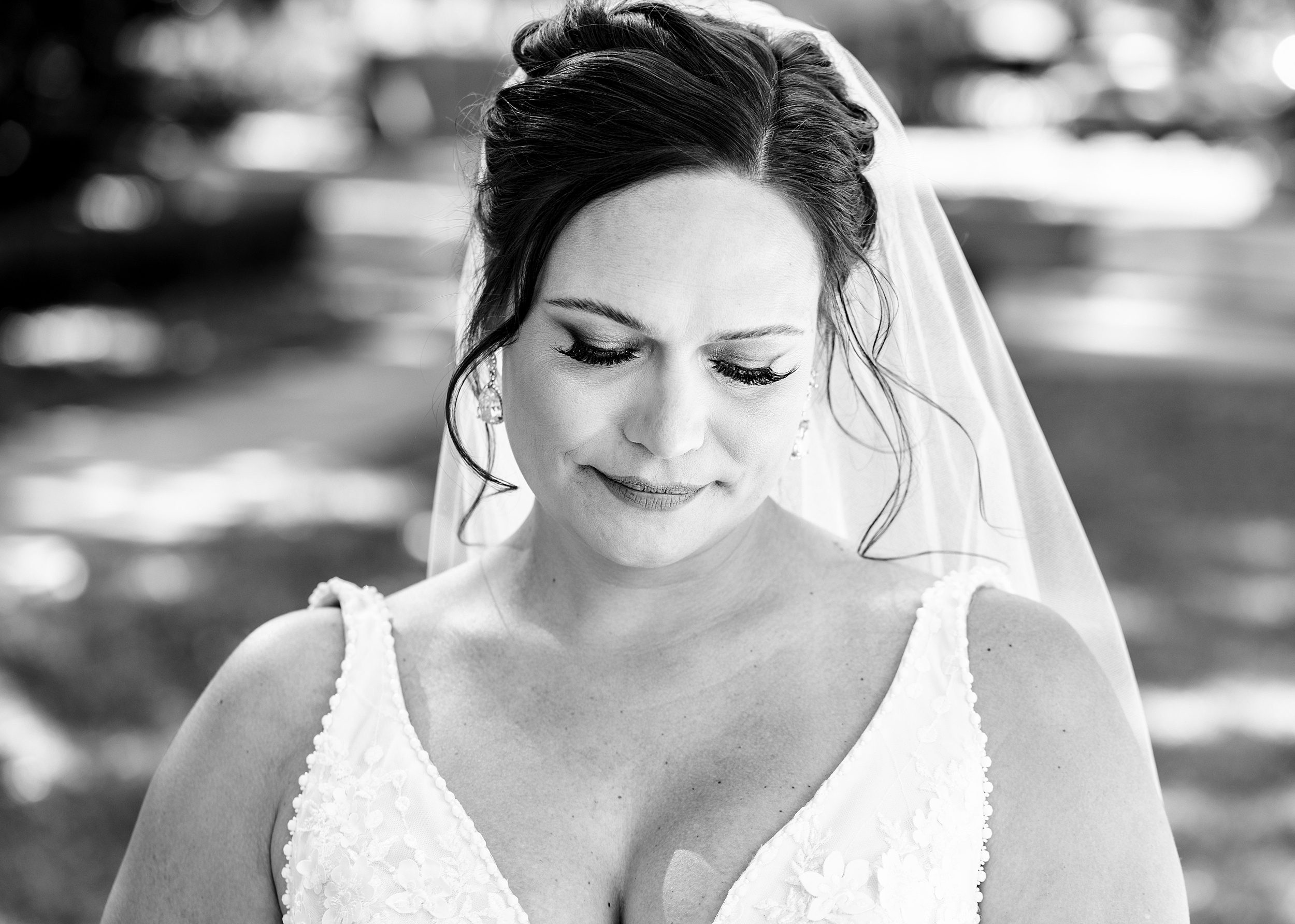 A bride smiles while standing outside in a lace embroidered dress