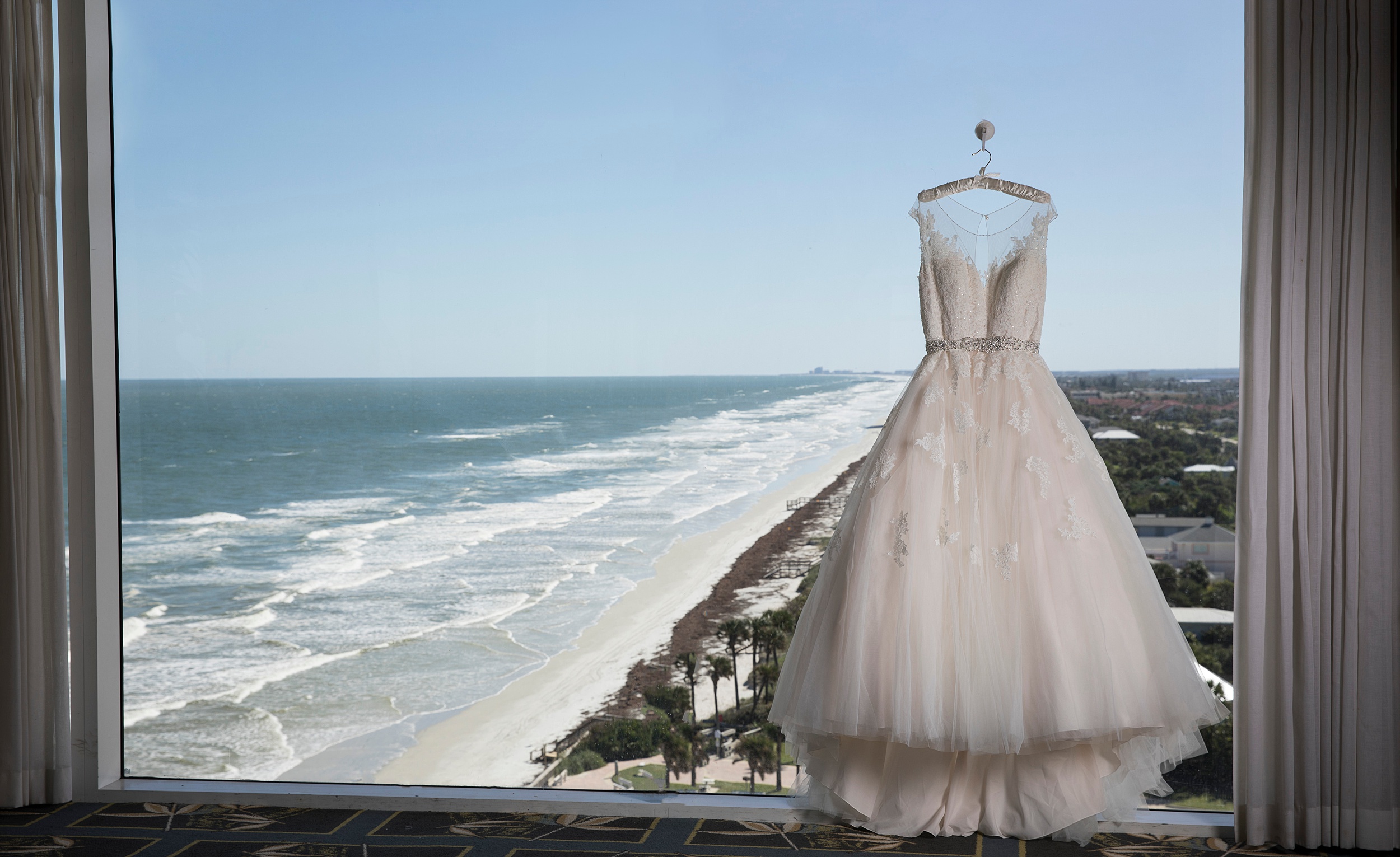 A dress hangs in a window overlooking the beach at a the shores resort and spa wedding
