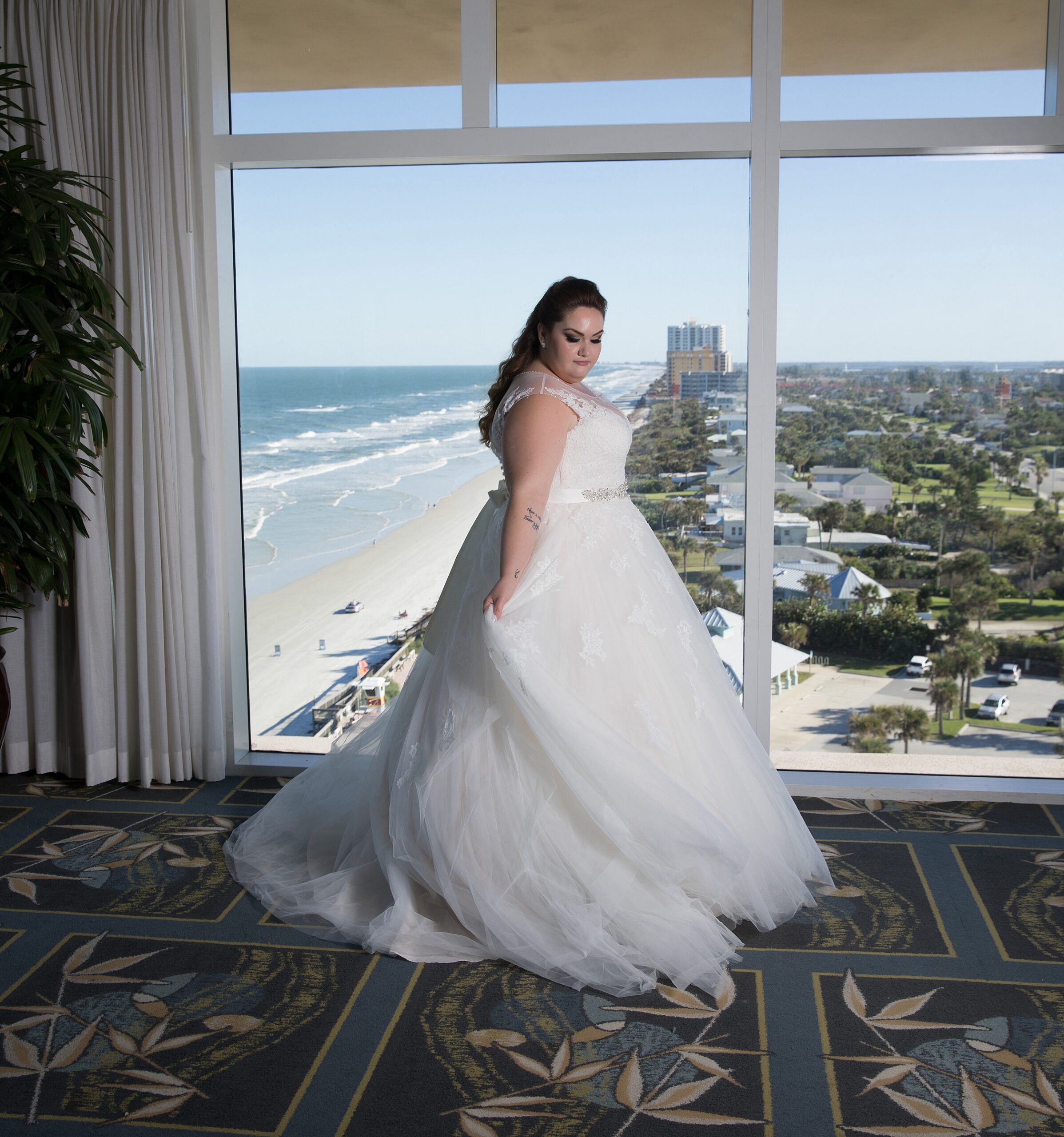 A bride twirls while showing off her dress in a high rise beach front hotel room