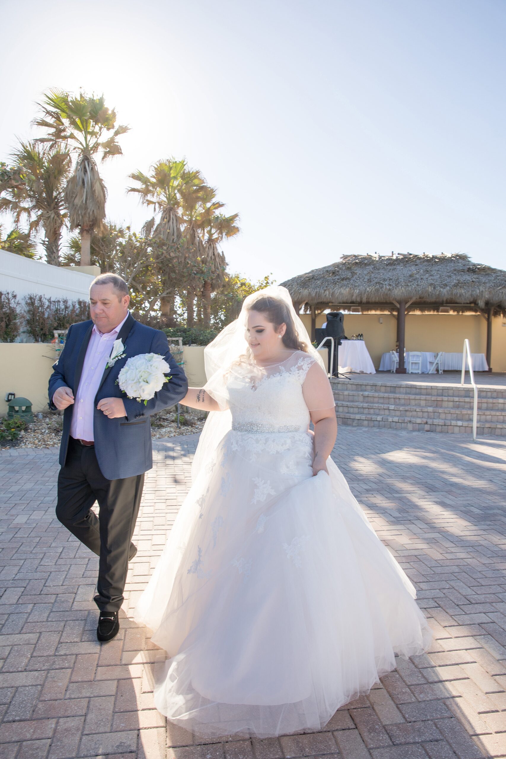 A father walks his daughter down the poolside aisle of her wedding ceremony