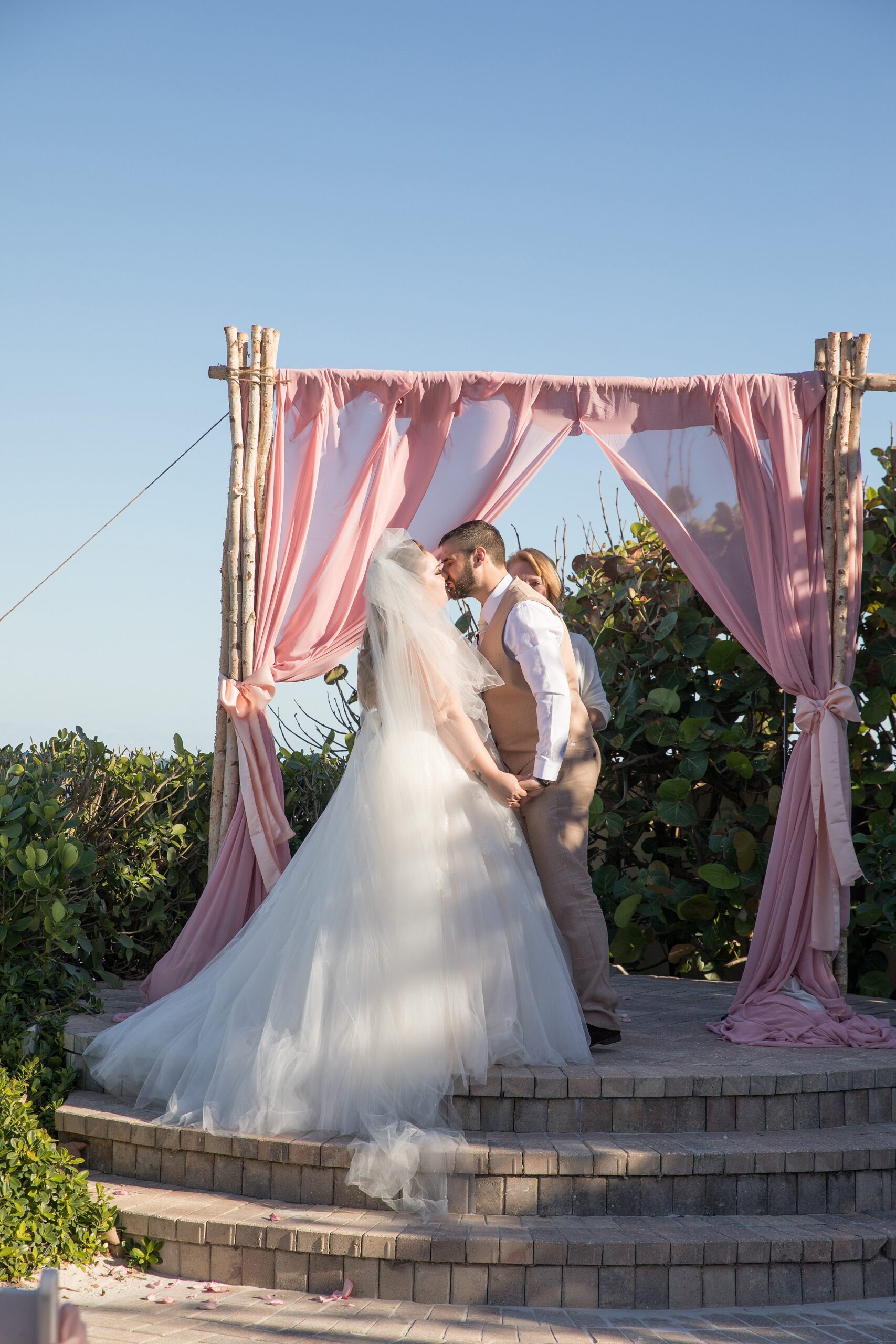 Newlyweds kiss at their the shores resort and spa wedding ceremony under a pink linen covered arbor