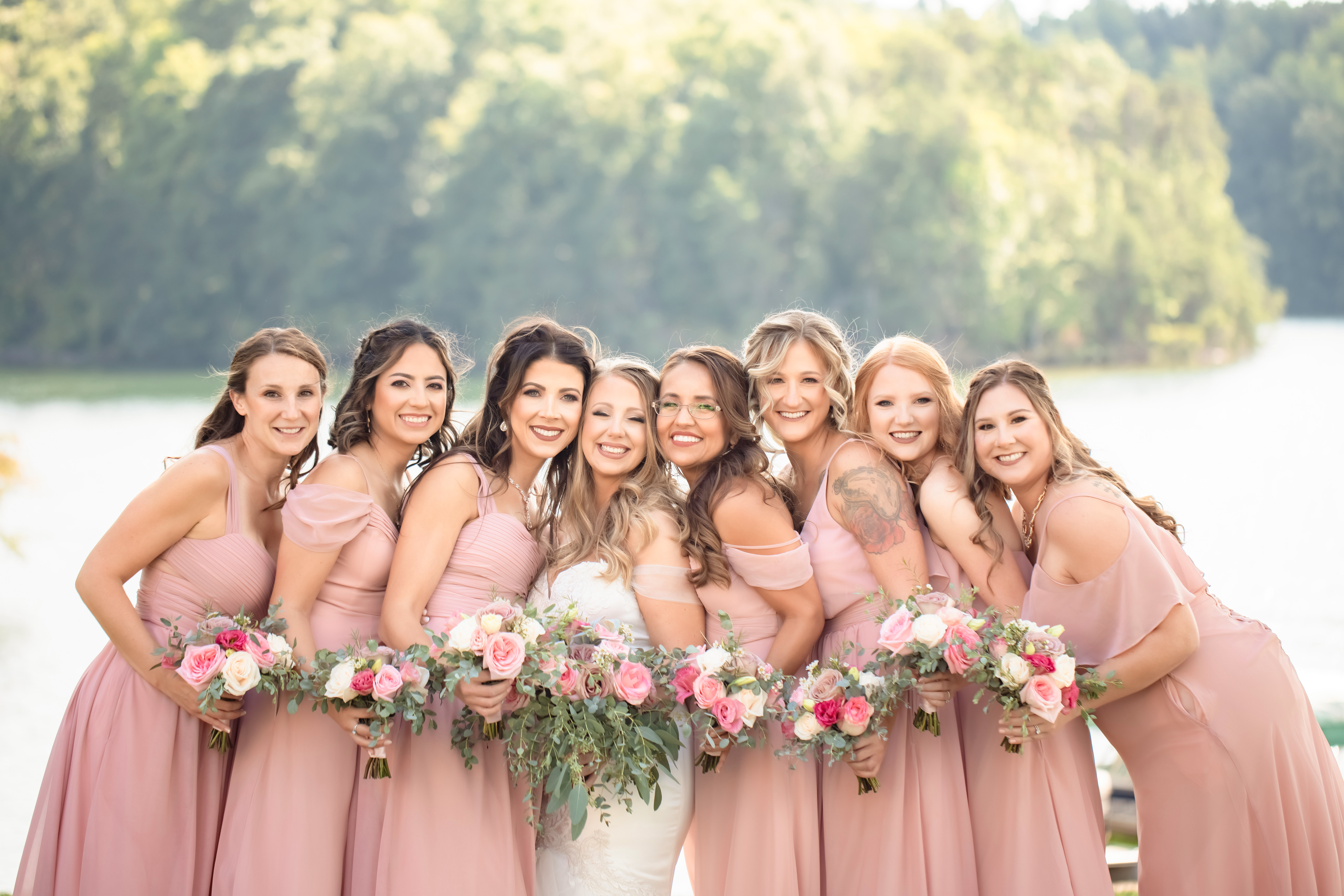 A bride stands cheek to cheek with her bridal party in pink dresses at her the tringali barn wedding