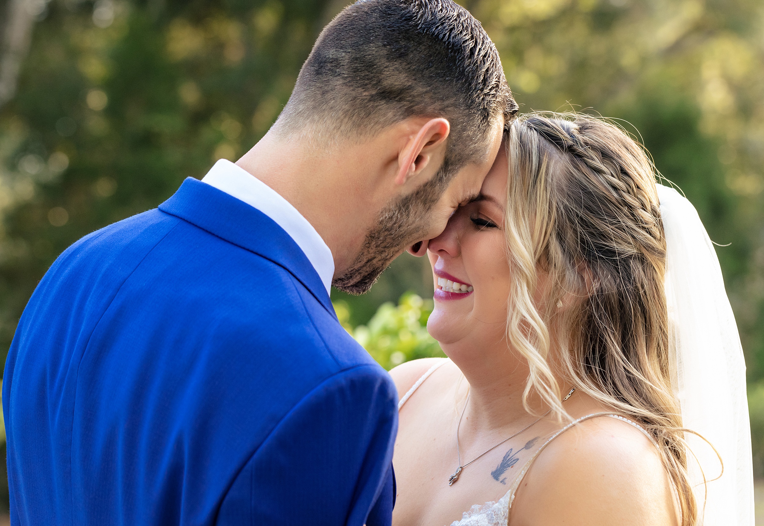 A groom in a blue suit touches foreheads with his bride in a lace dress