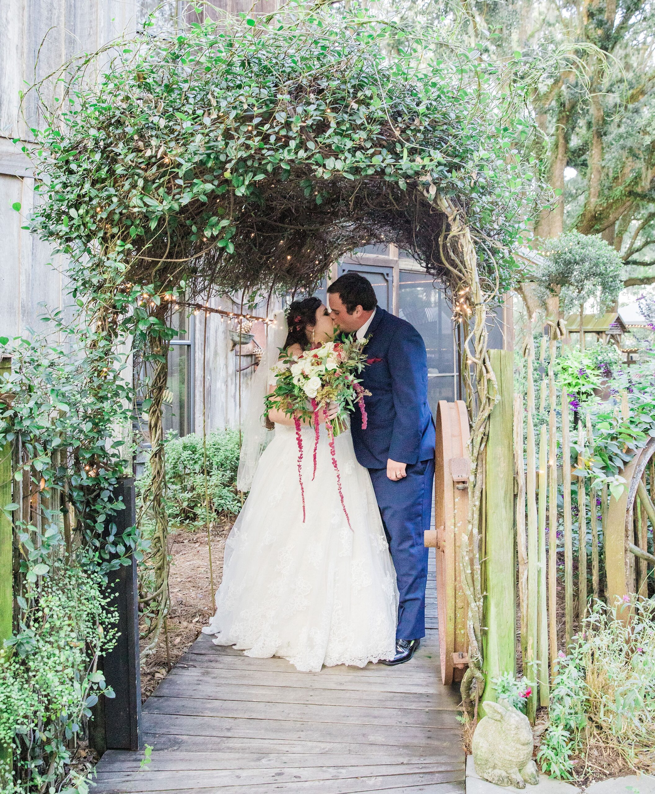 Newlyweds kiss under a vine covered archway strung with strig lights