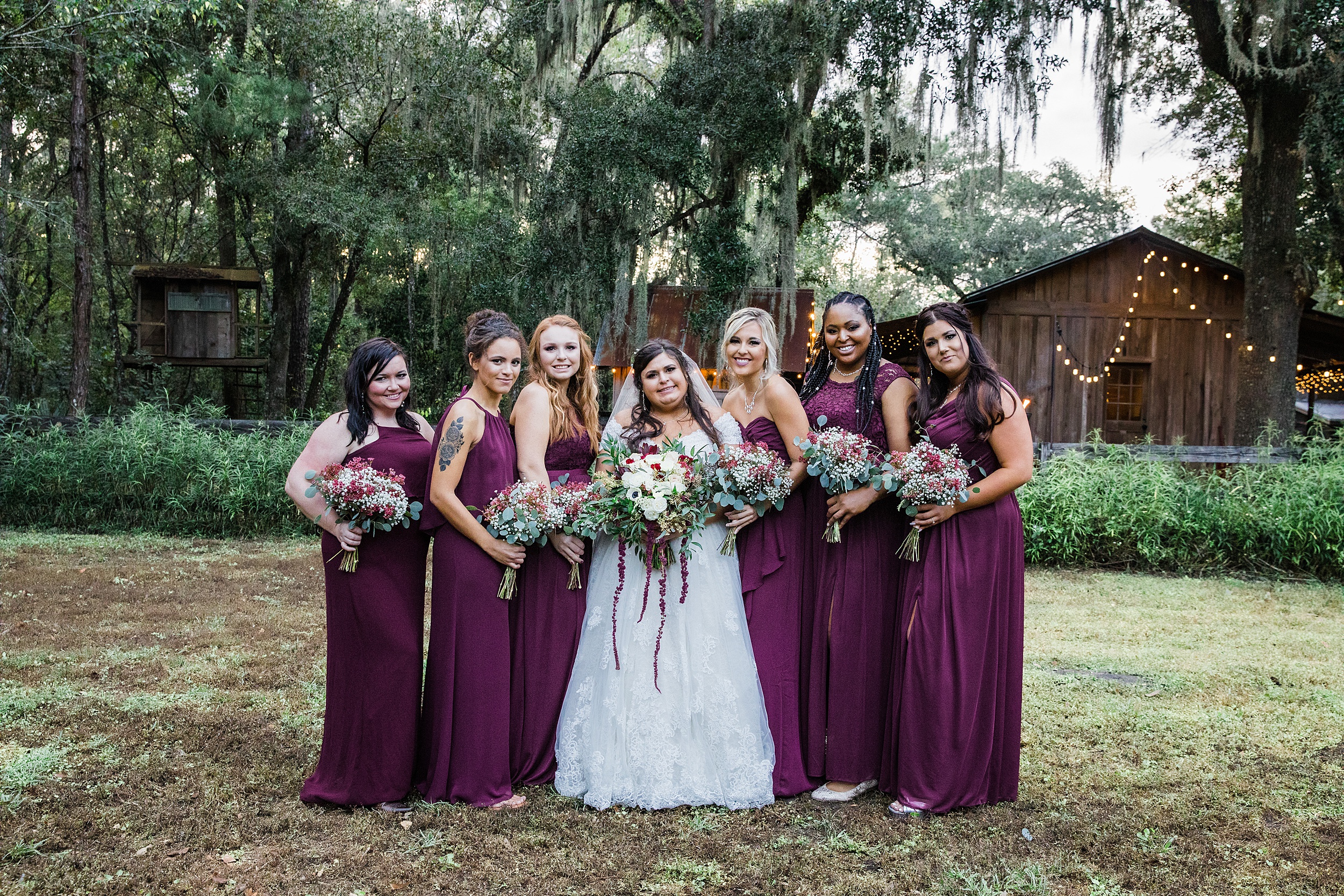 A bride stands with her bridesmaids all in purple dresses and holding bouquets