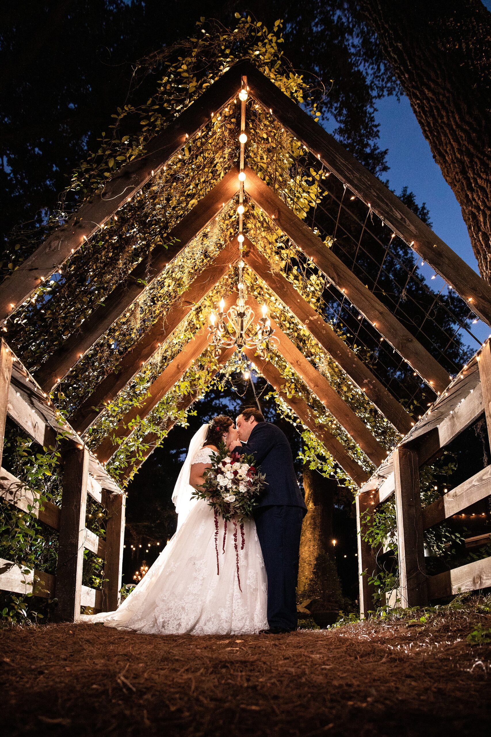 Newlyweds kiss under a large trellace arch with a chandelier at their tucker's farmhouse wedding