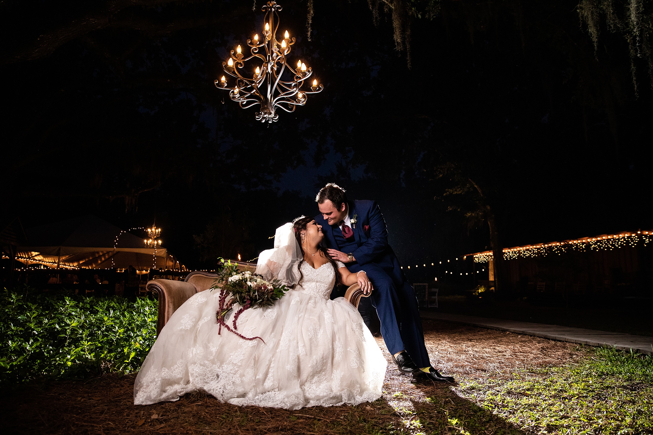 Newlyweds share a quiet moment on a vintage couch under an outdoor chandelier at night at their tucker's farmhouse wedding