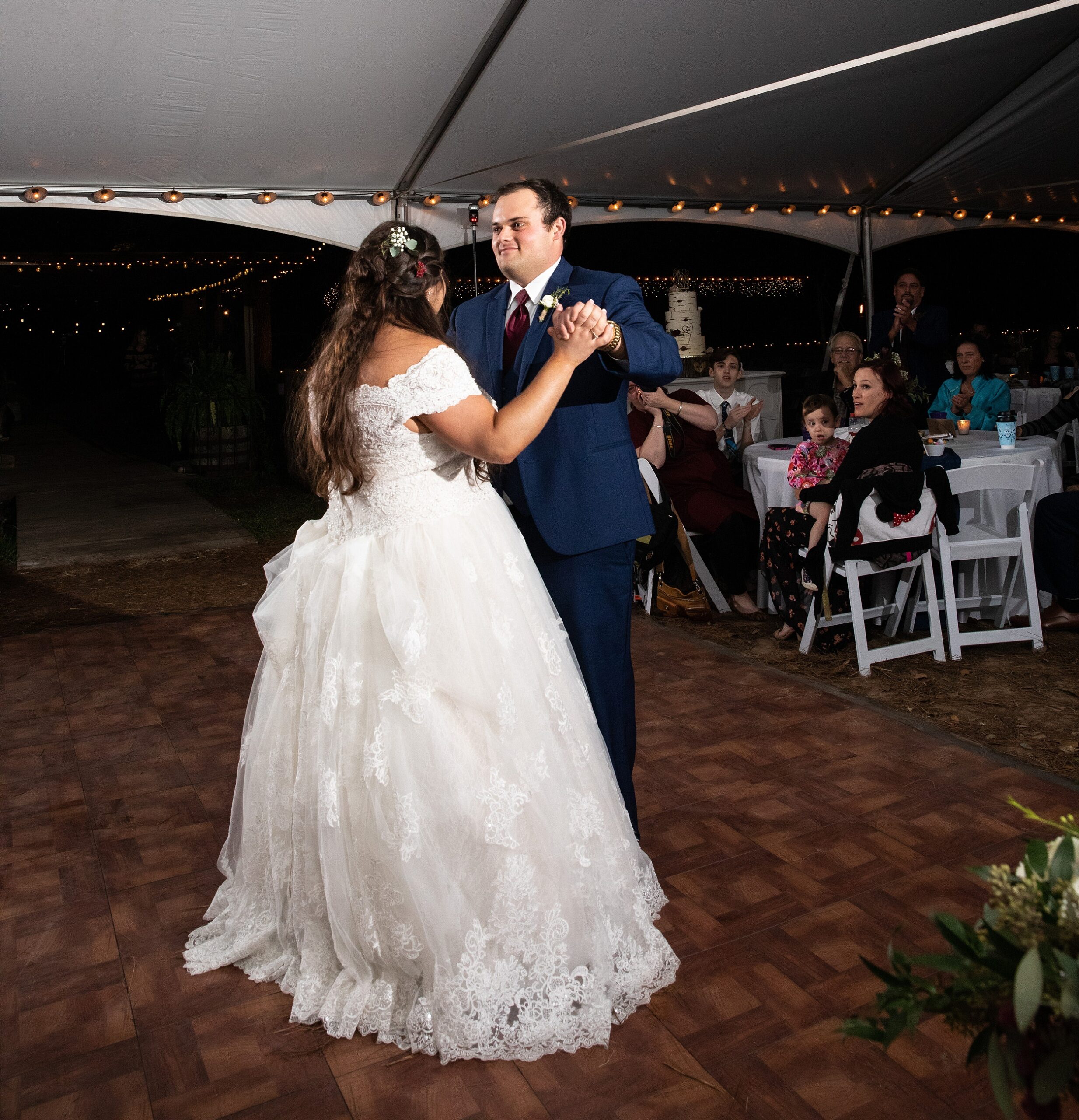 Newlyweds dance under a large white tent with guests watching