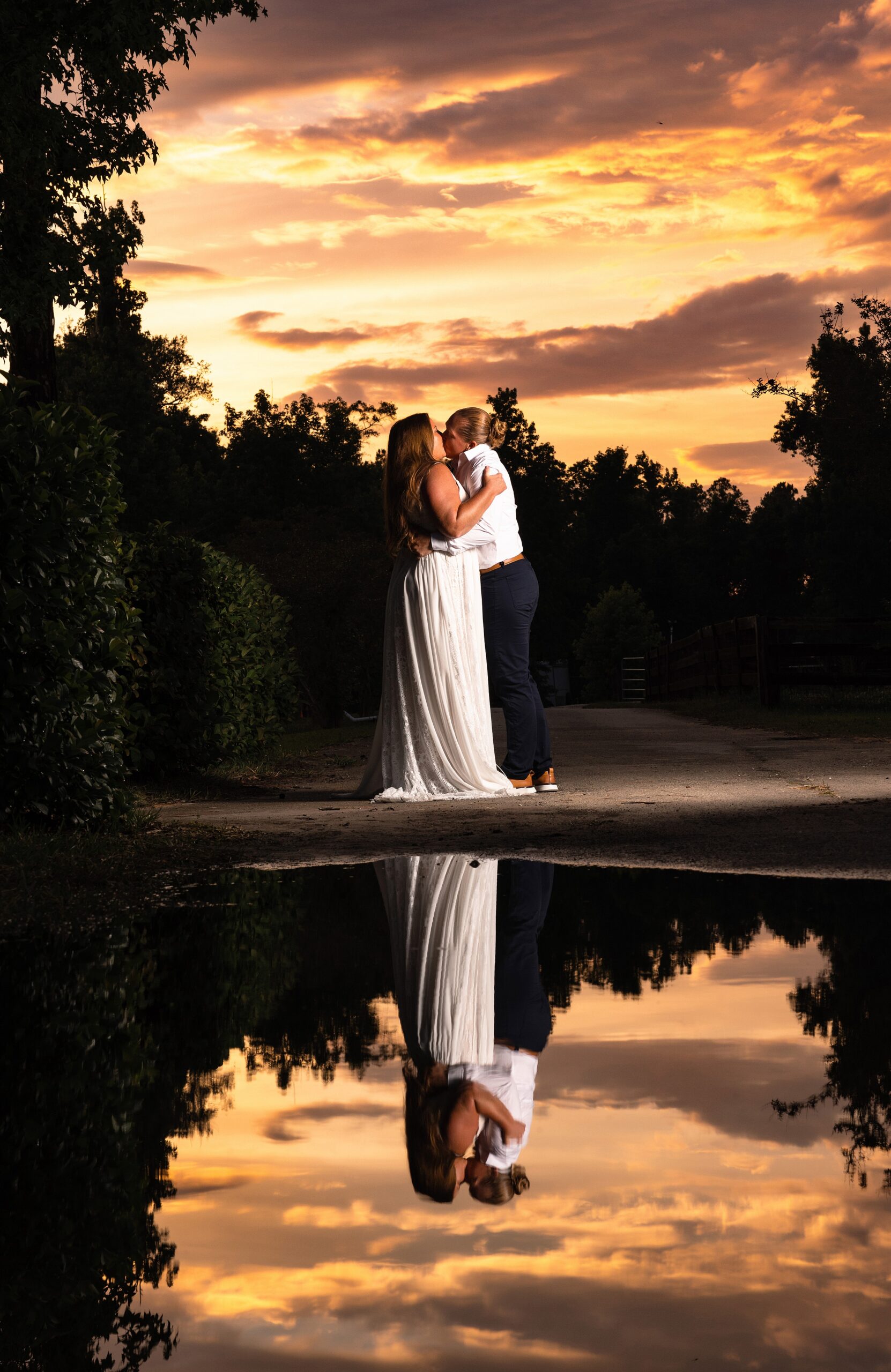 Newlywed brides kiss by a garden pond at sunset at their marsh landing country club wedding