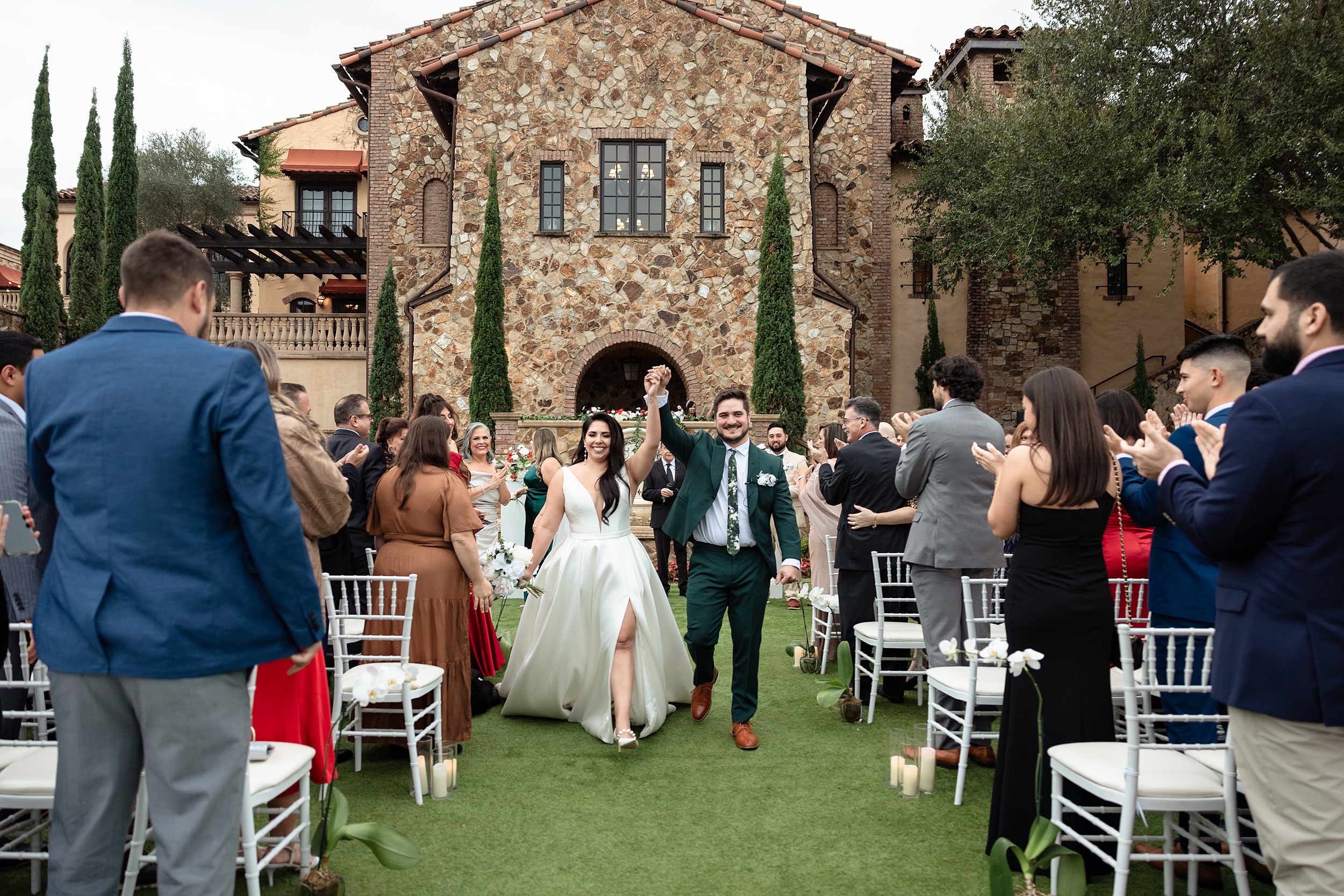 Newlyweds celebrate with hands up while walking up the aisle to applause from their guests