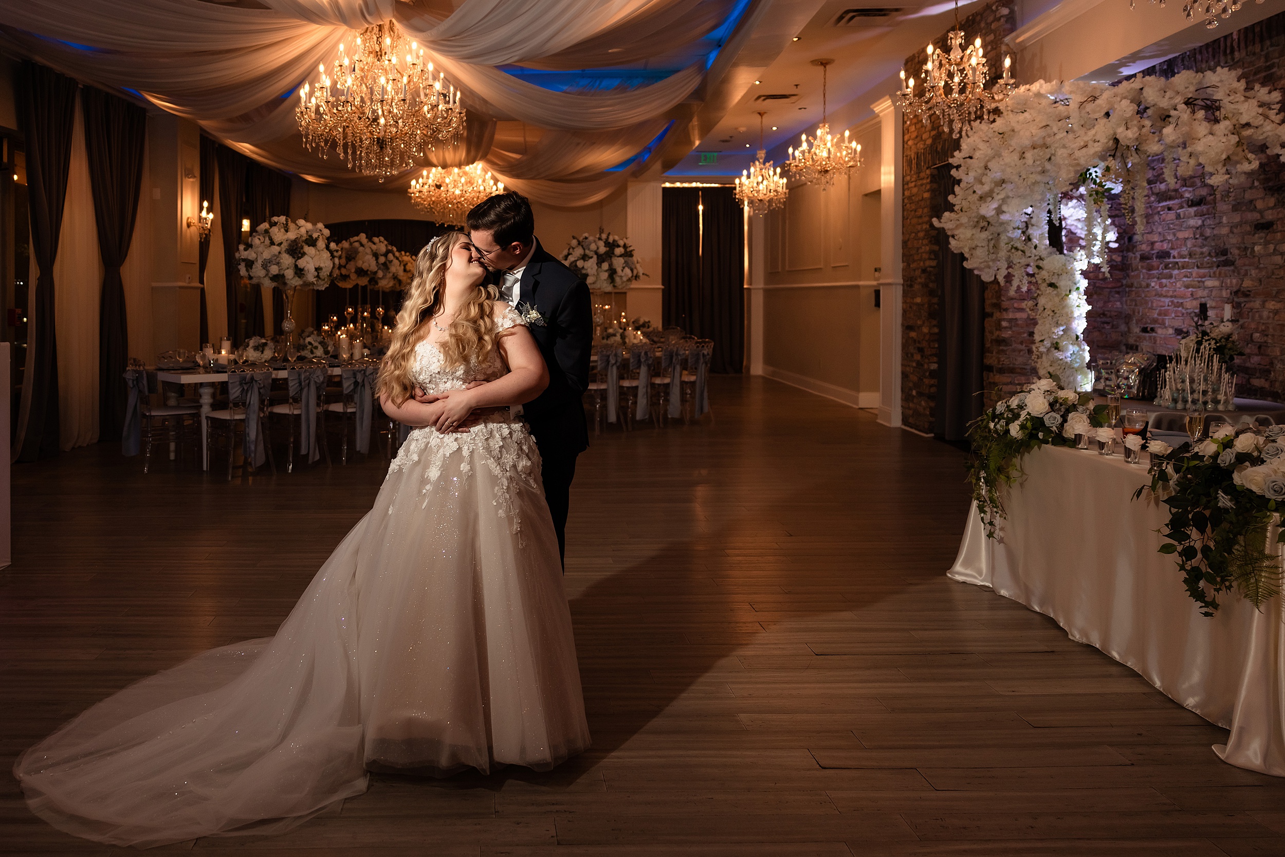 Newlyweds share a kiss inside their empty reception ballroom covered in flowers and chandeliers