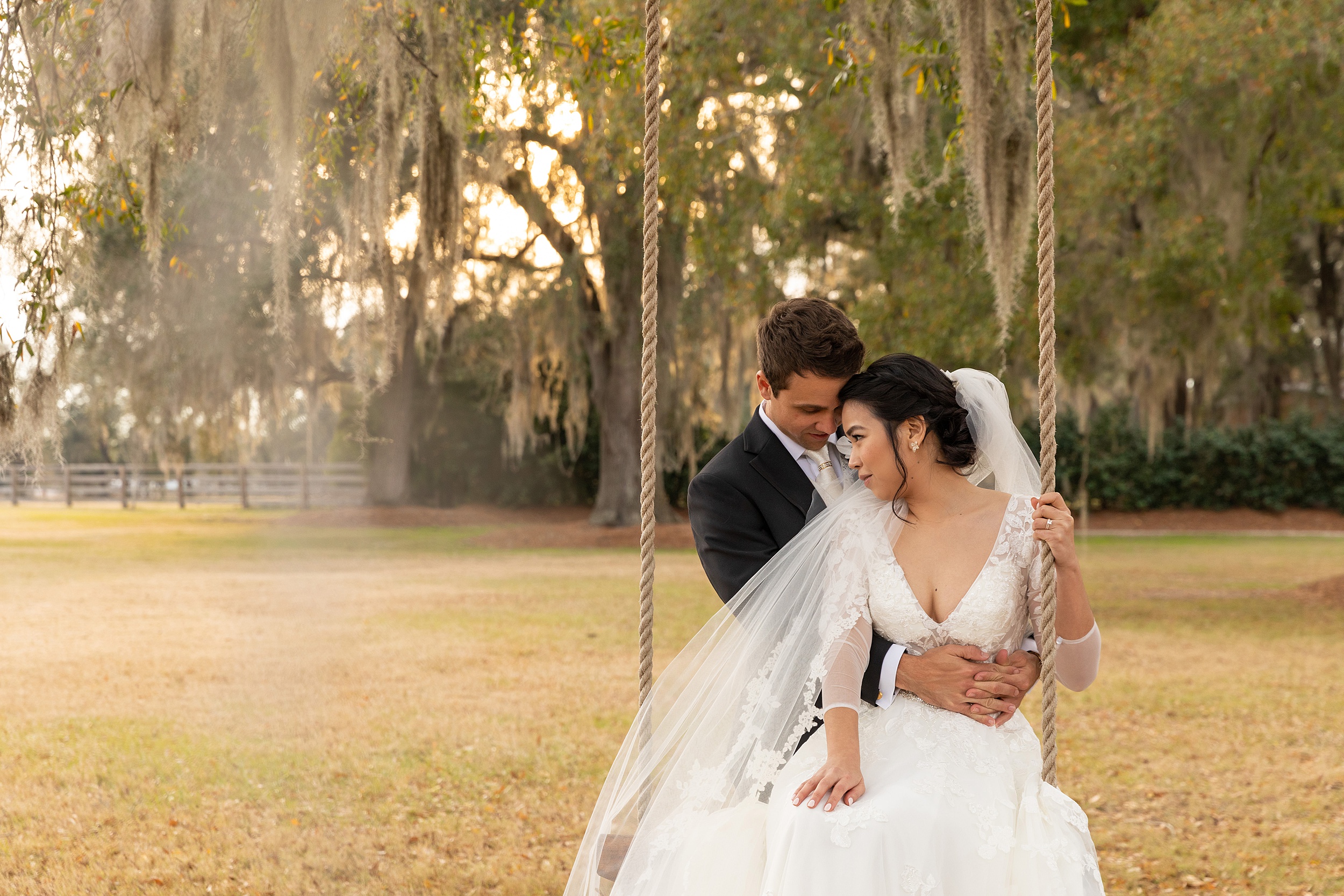 A bride sits on a swing in a park lawn while being hugged by her groom at sunset at one of the orlando wedding venues