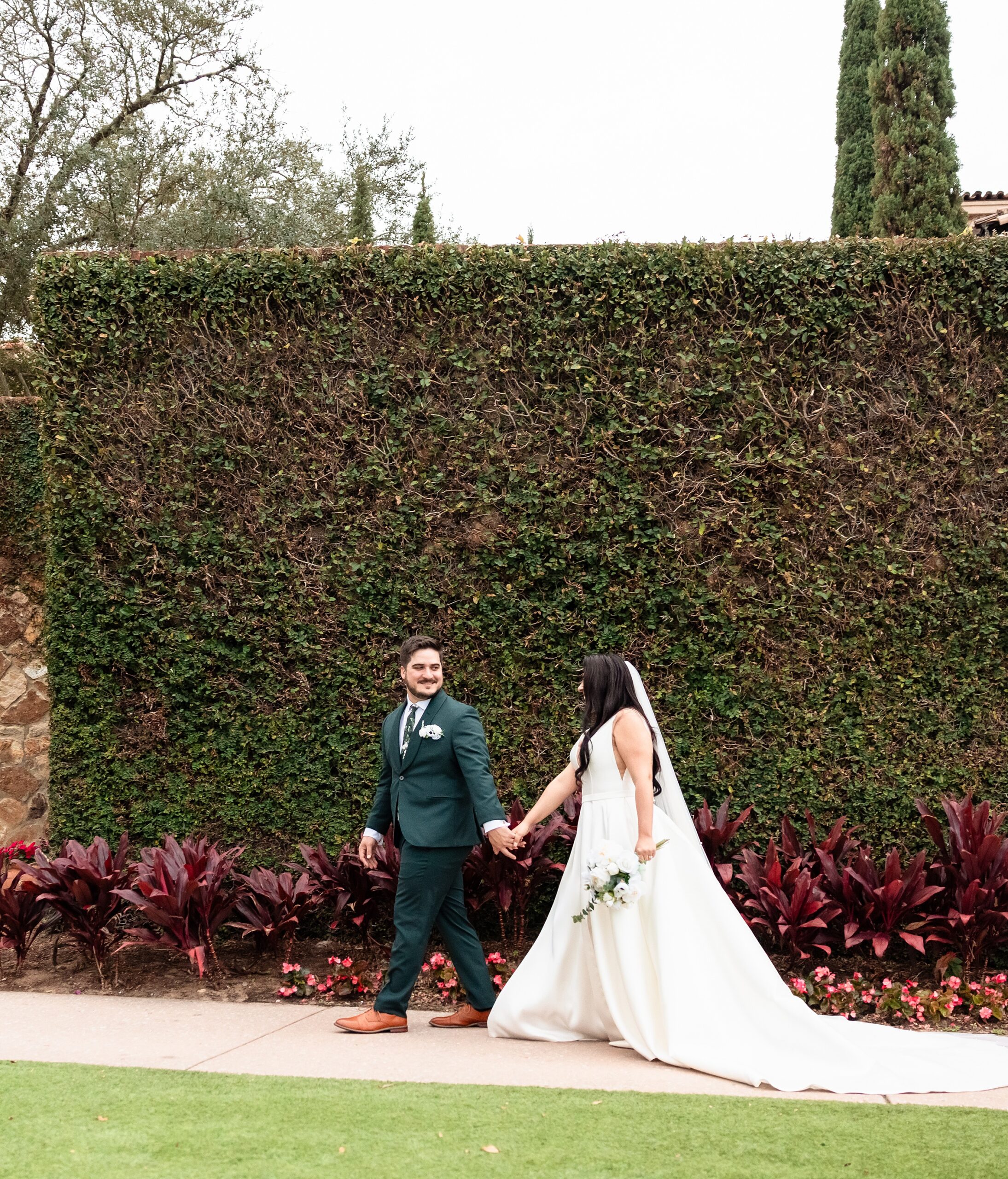 A groom in a green suit leads his bride up a garden sidewalk by the hand thanks to st augustine wedding planners