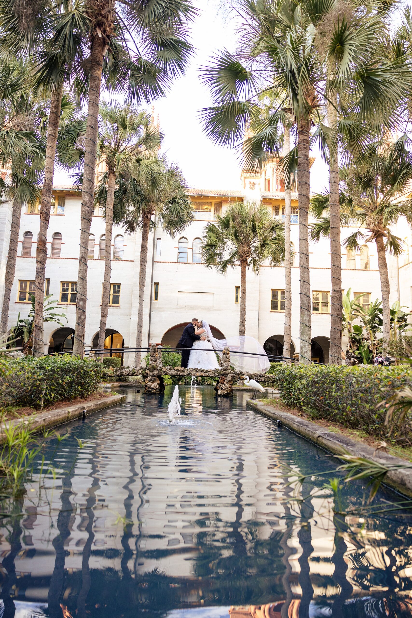 Newlyweds kiss on a bridge over a pond and fountain thanks to their st augustine wedding planners