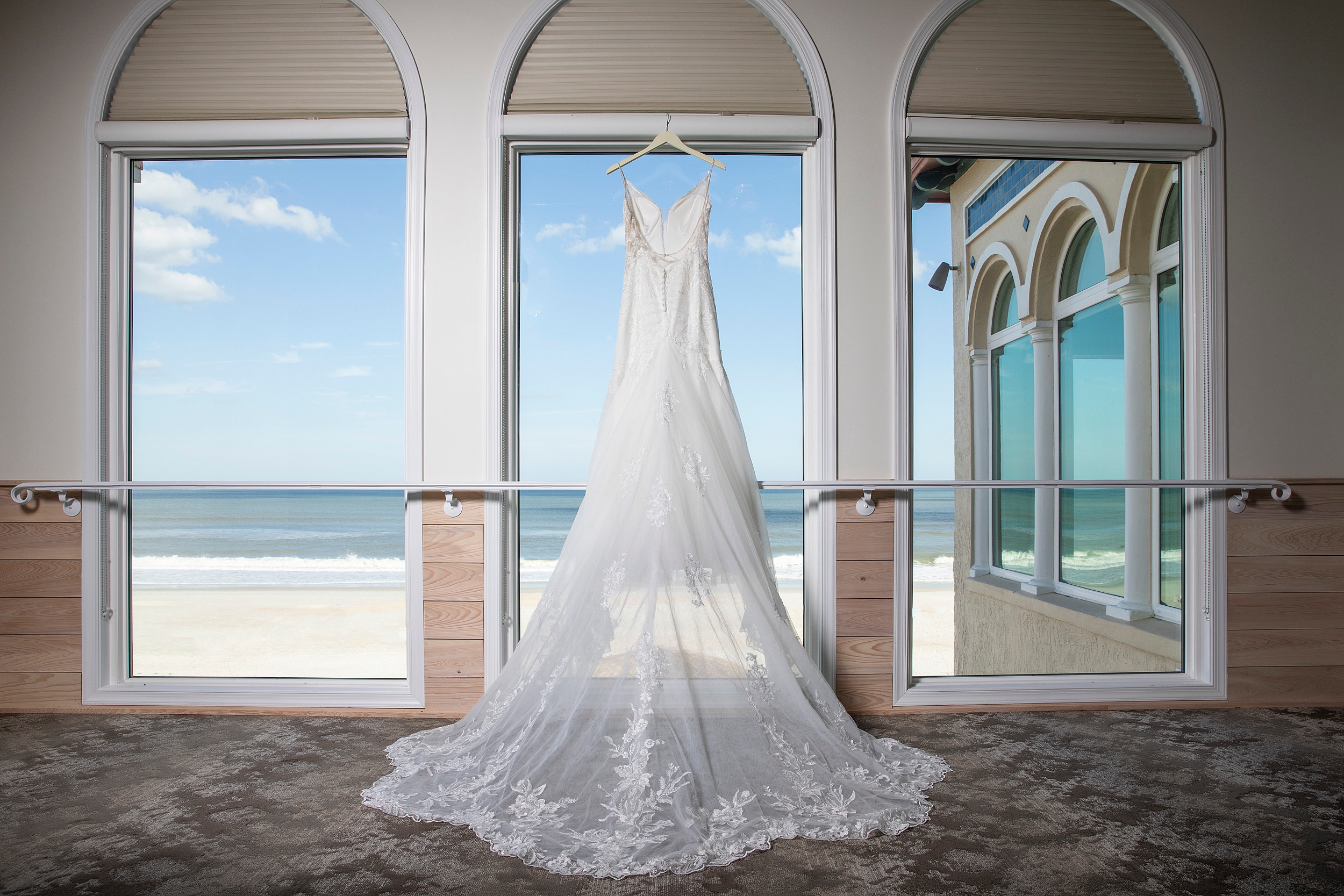 A wedding dress hangs in a window overlooking a beach