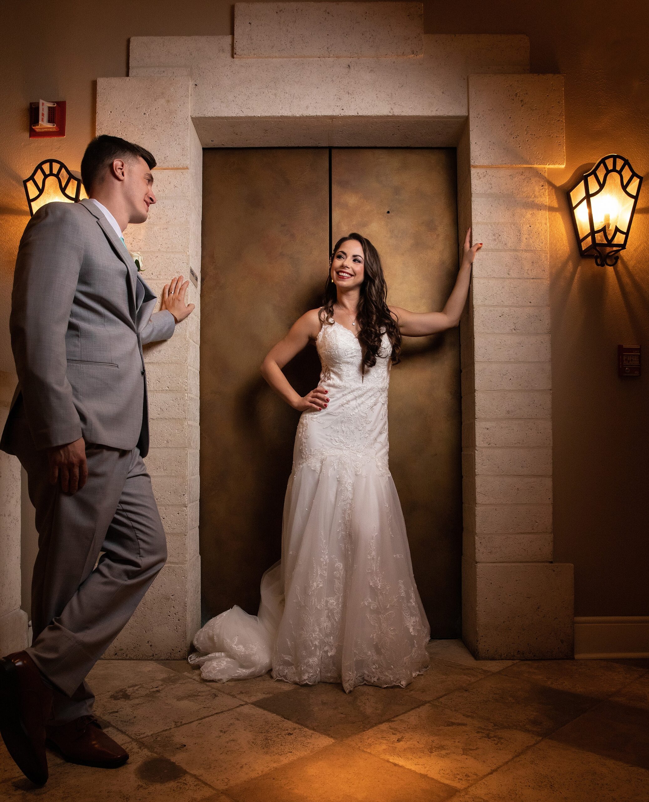 A bride stands in the elevator entrance at the lodge and club ponte verda wedding venue as her groom leans on the wall smiling at her