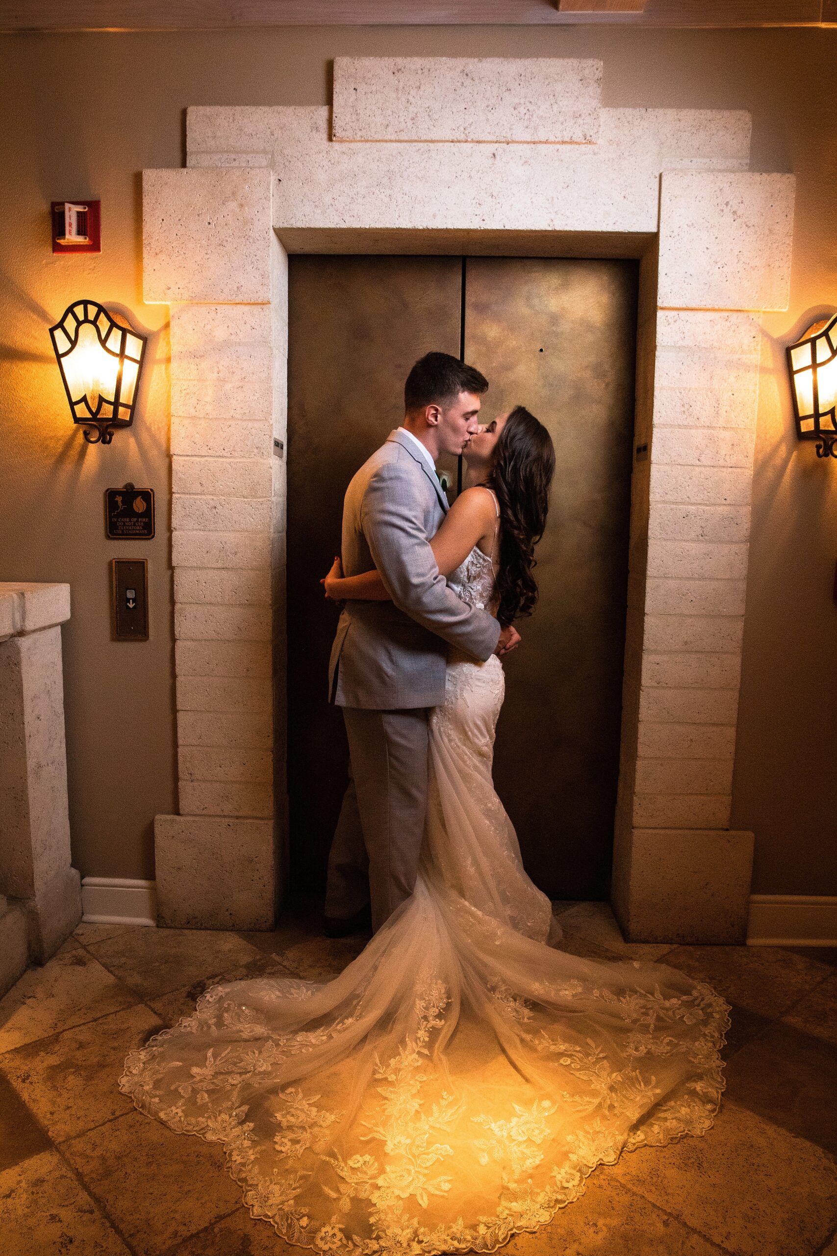 Newlyweds kiss in front of a stone framed elevator door
