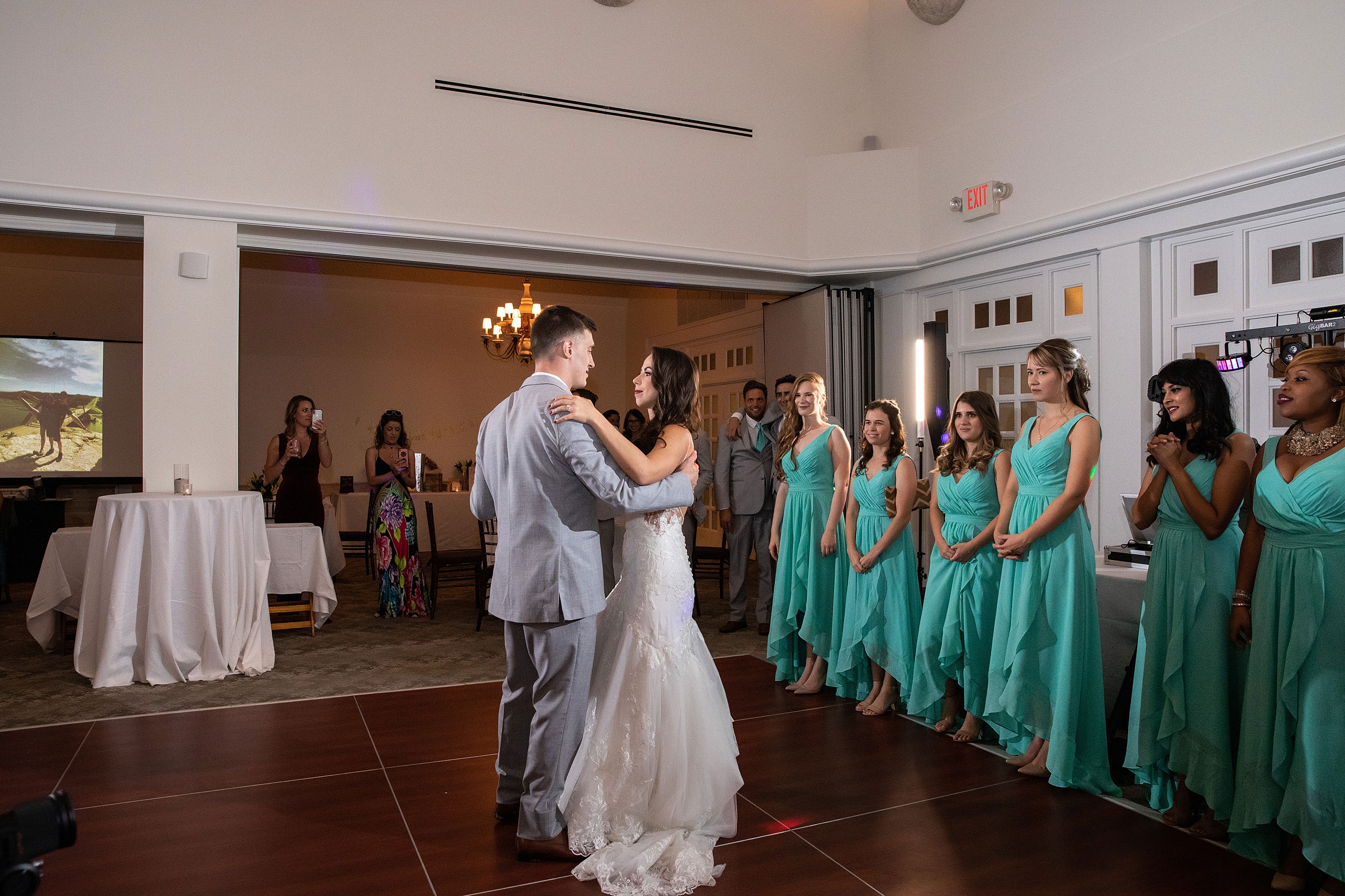 Newlyweds dance close during their first dance as the wedding party looks on