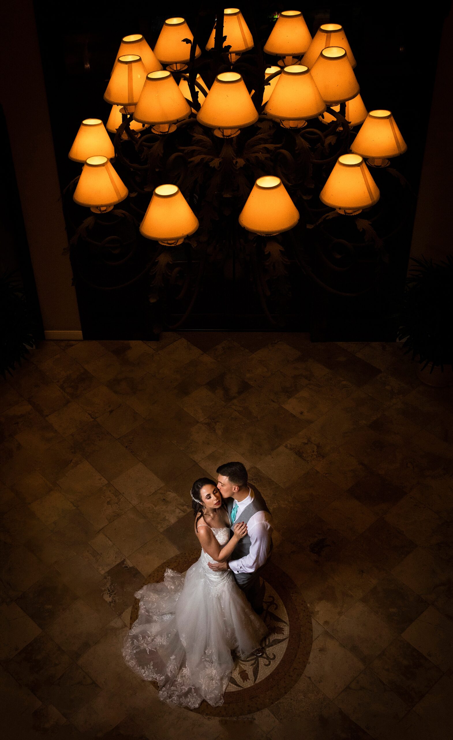 Newlyweds share a quiet kiss under a chandelier in the foyer at their the lodge and club ponte verda wedding