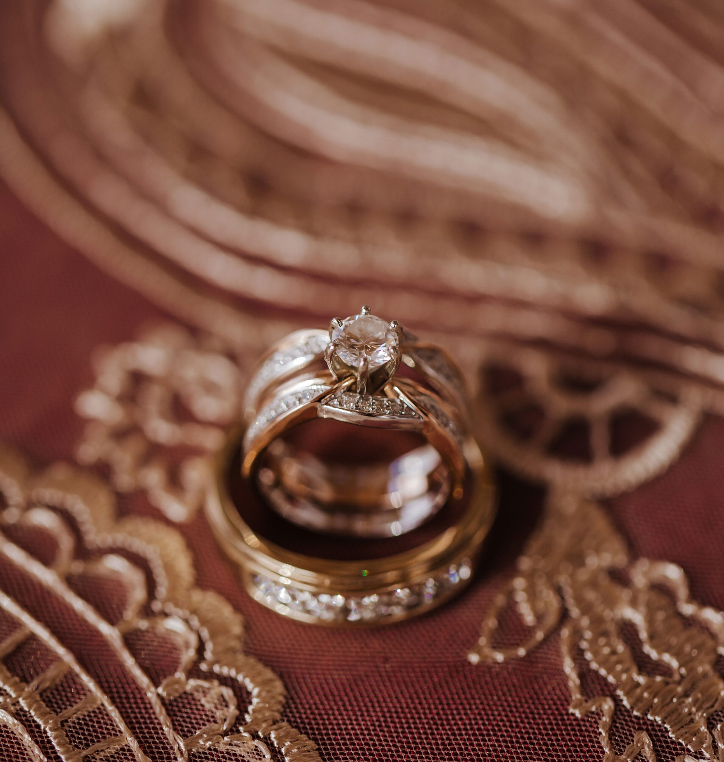 Details of wedding rings standing on a red and gold embroidered tablecloth