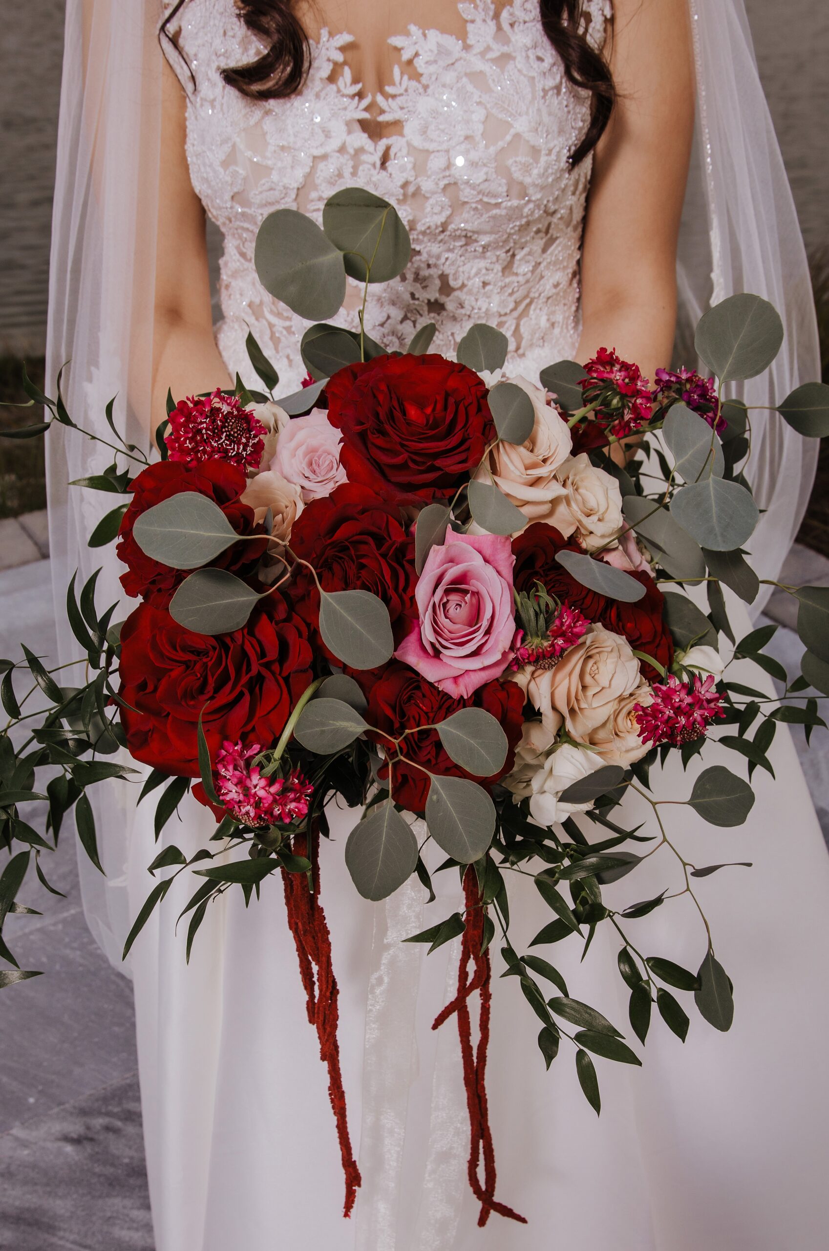 Details of a bride in a lace dress holding her bright red and pink rose bouquet at her the manor at 12 oaks farm