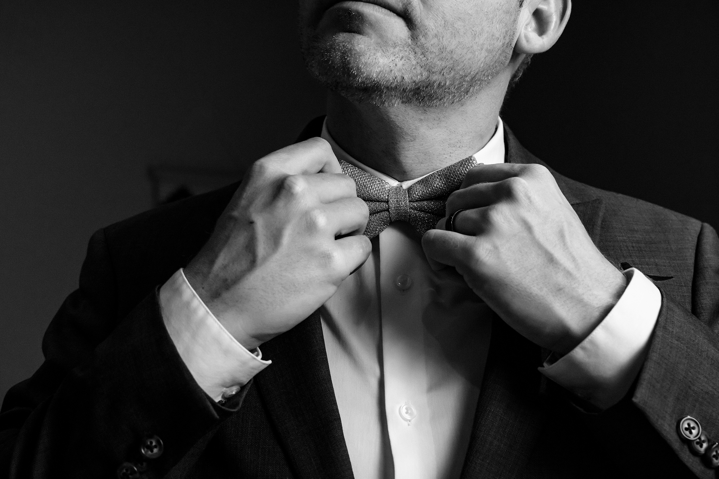A groom adjusts his bowtie while standing in a window at his heathrow country club wedding