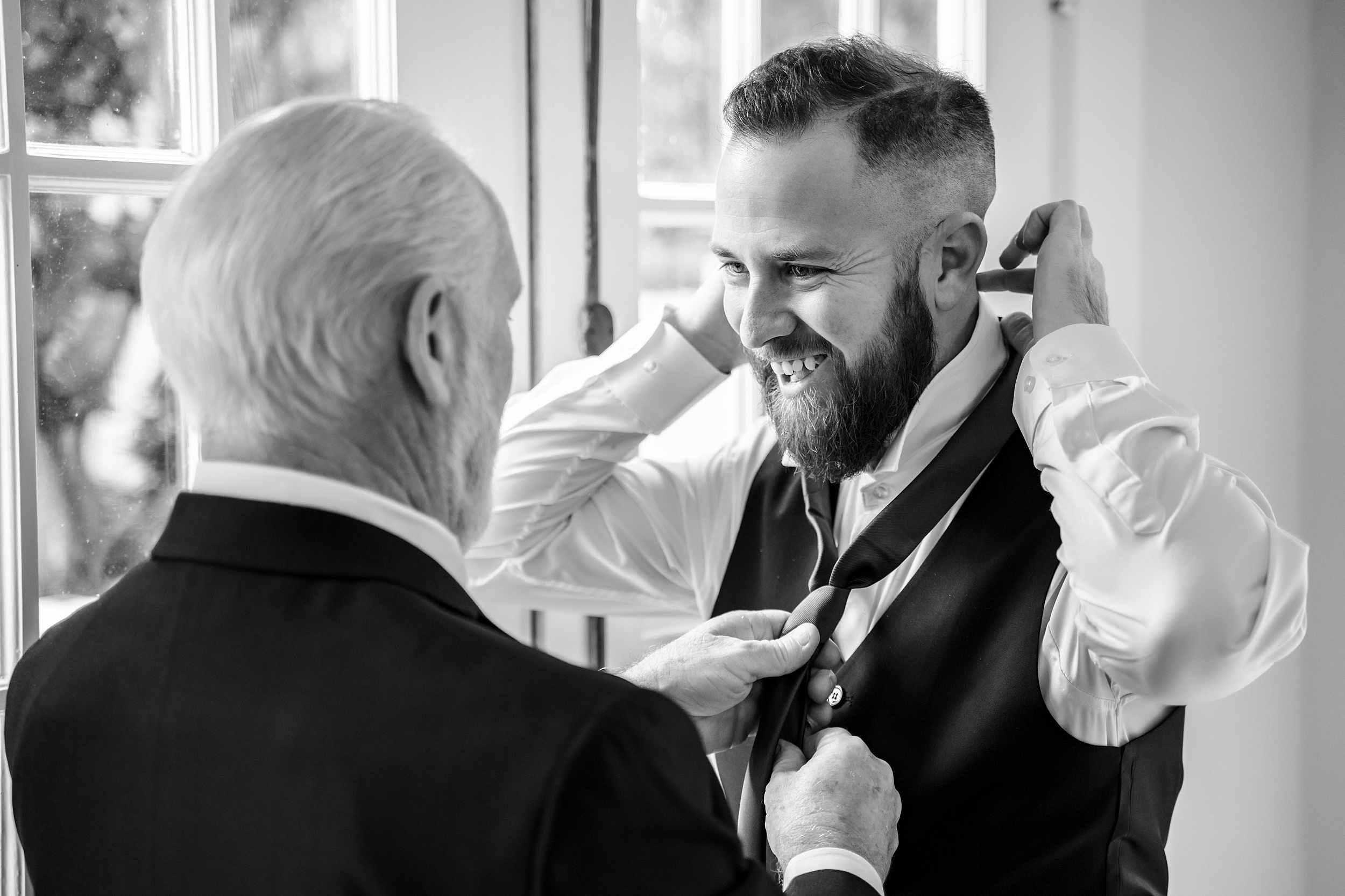 A groom gets help from dad to put on his tie in a getting ready room